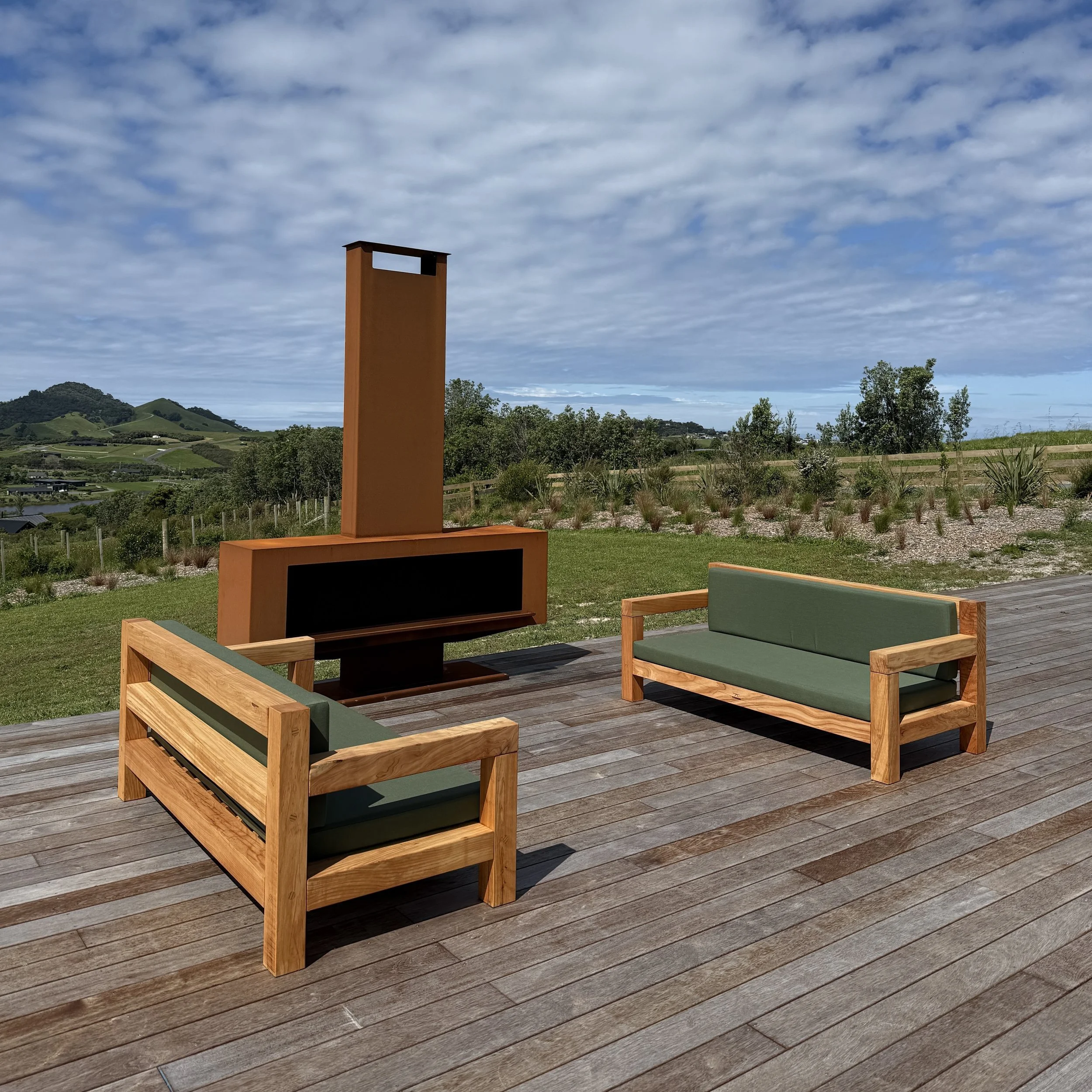 Macrocarpa outdoor lounge seating with green squabs around an outdoor fireplace.
