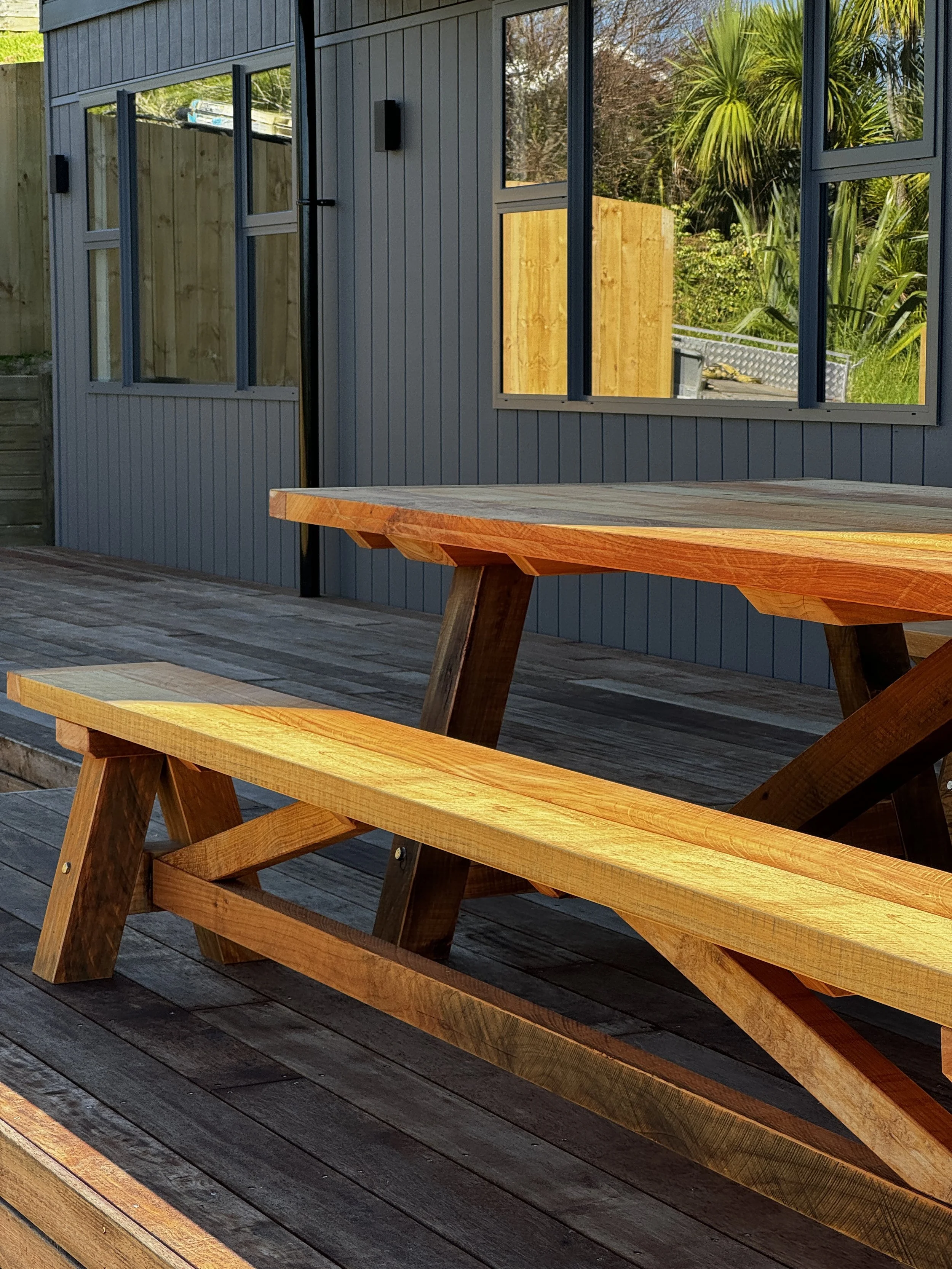 Macrocarpa outdoor dining table with matching bench seat on a timber deck.