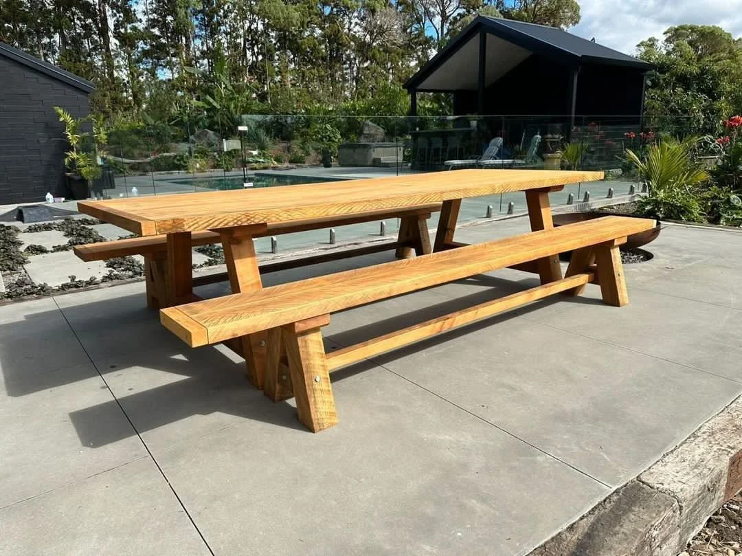 Large Macrocarpa outdoor dining table with matching bench seats beside a pool.