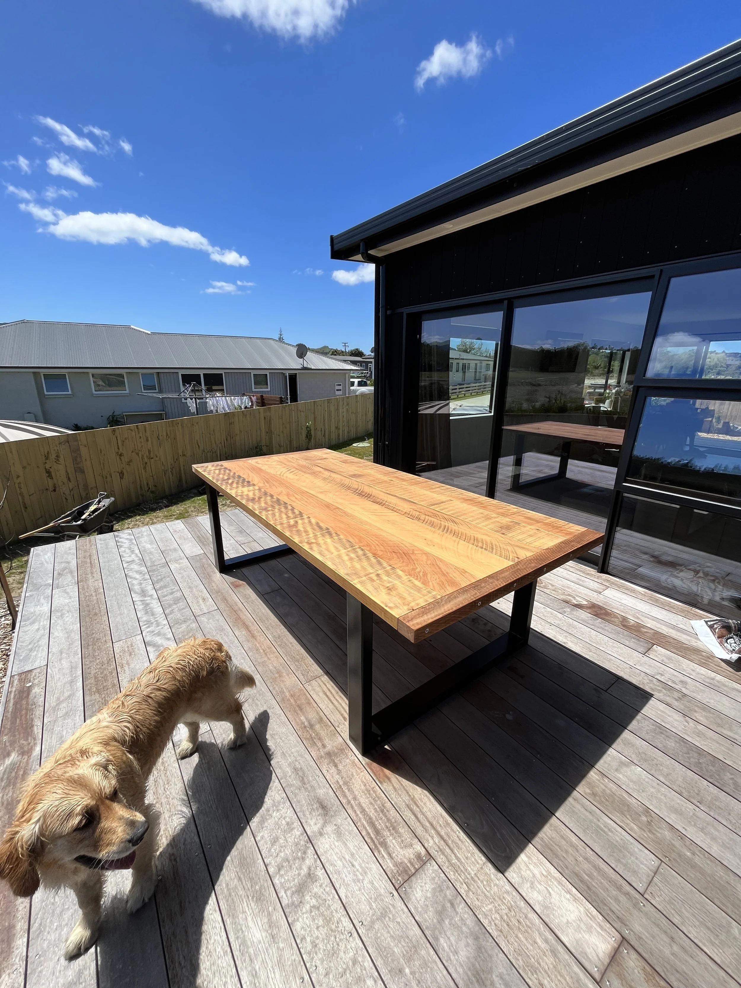 Macrocarpa dining table with black steel frame on a sunny outdoor deck.