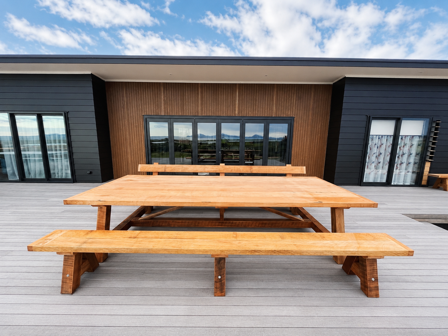Macrocarpa outdoor dining table and matching benches on the deck of a modern home.
