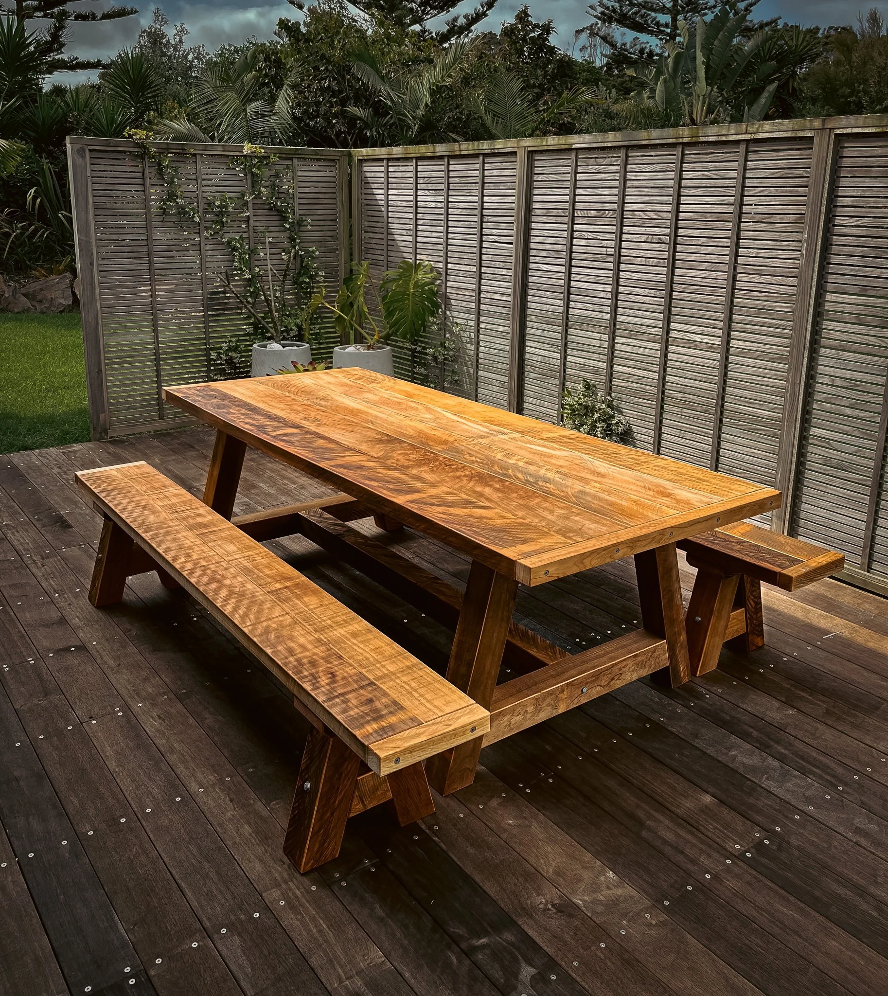 Macrocarpa outdoor dining table and matching bench seats on a timber deck.