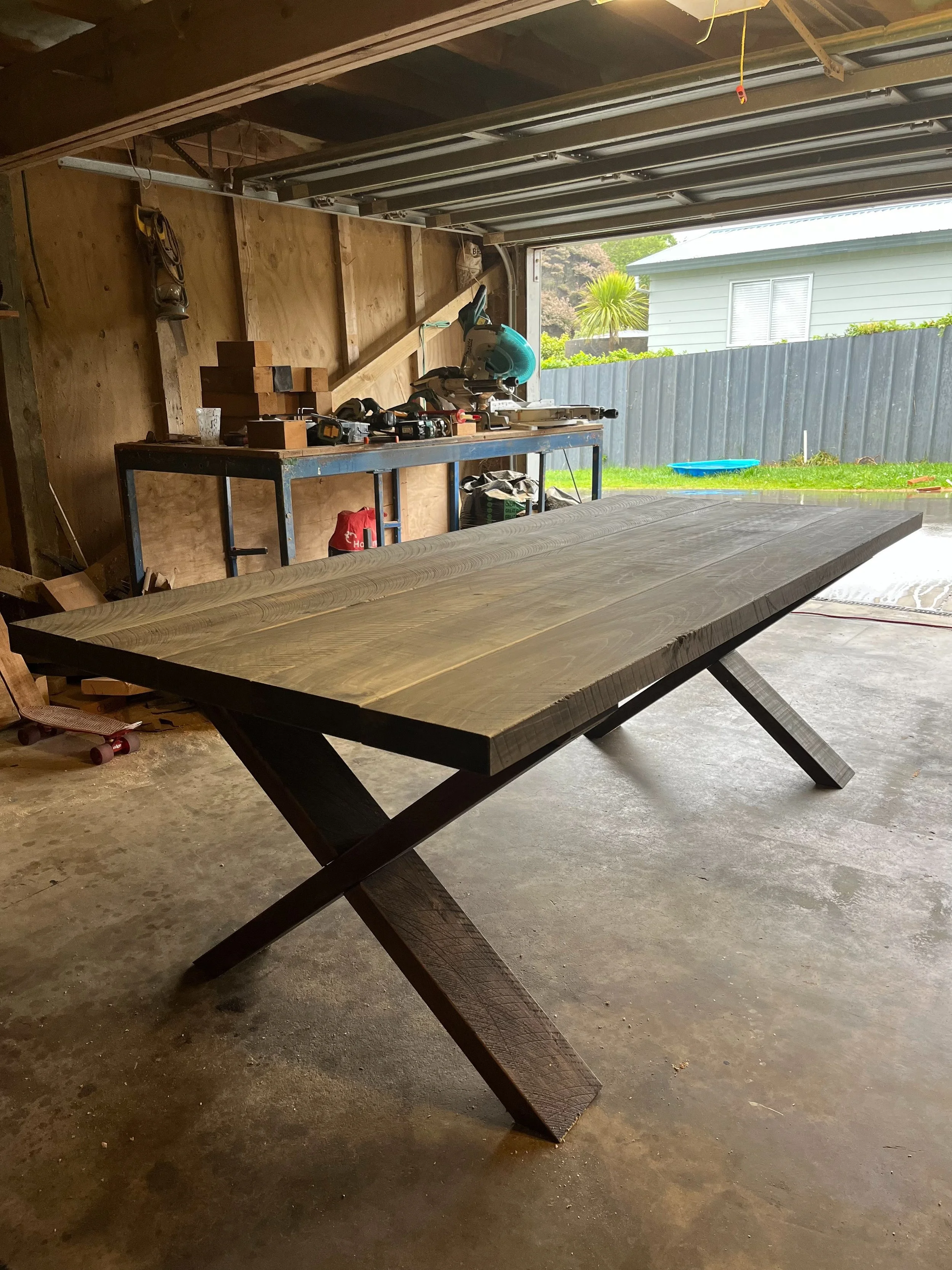 Dark-stained Macrocarpa dining table with X-shaped legs in the Benchmark Build workshop.