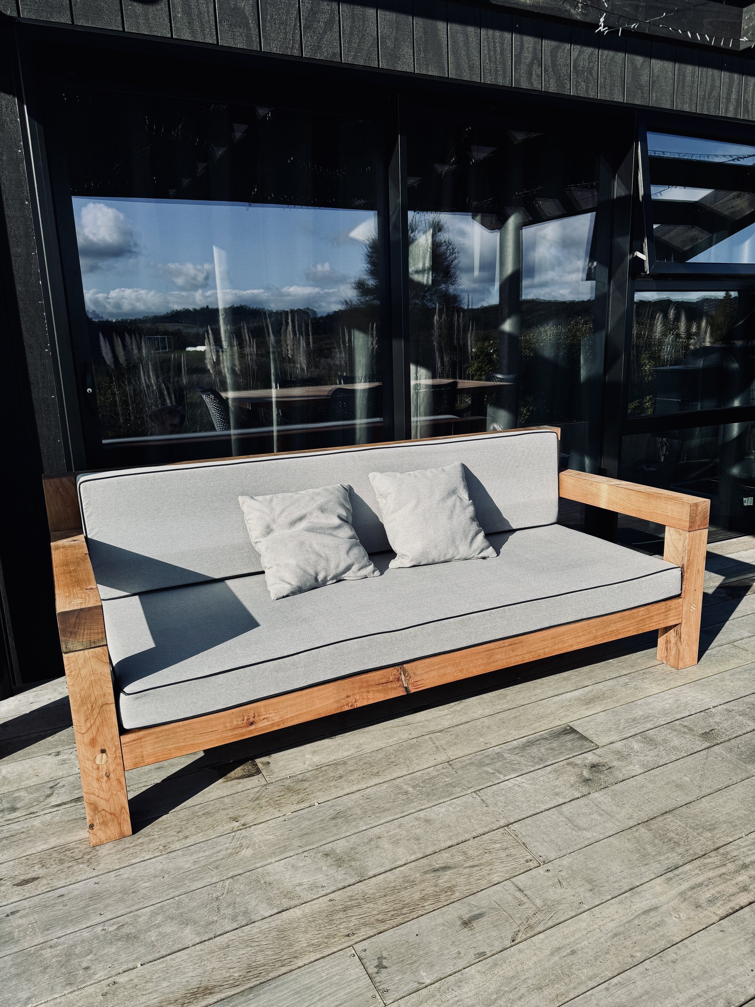 Macrocarpa outdoor lounge with grey squab cushions outside a modern home.