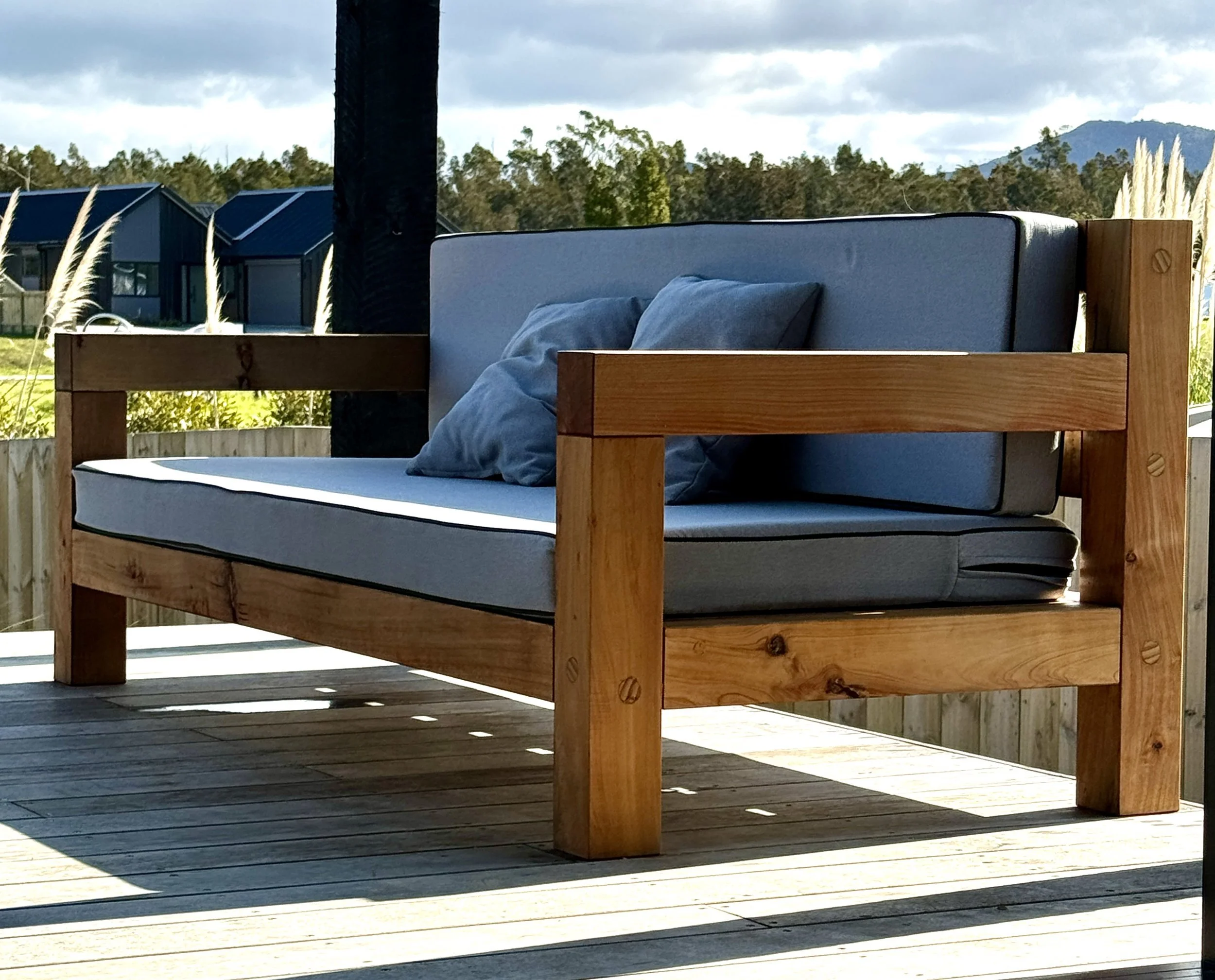 Macrocarpa outdoor lounge with grey squab cushions on a timber deck.