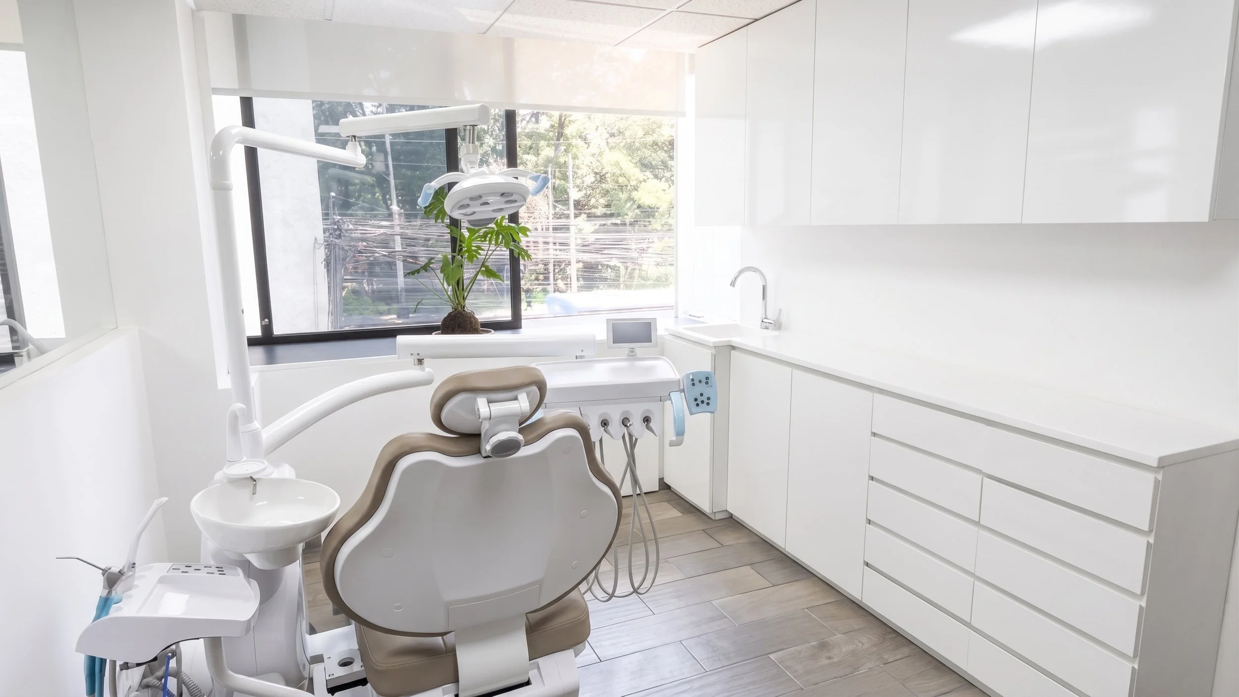 Modern dental office with dental chair, equipment, and a large window with a view of trees.