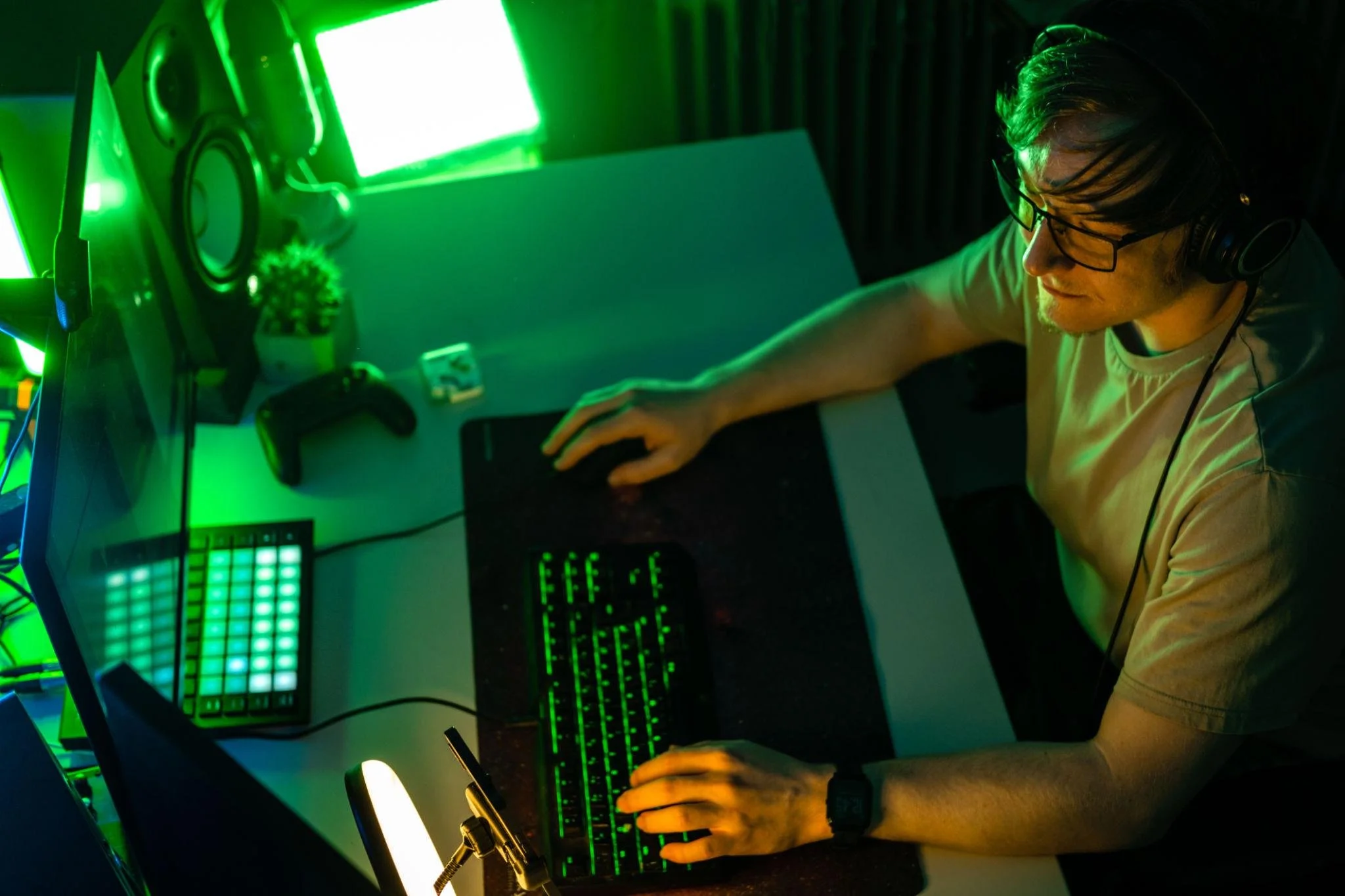 Person with glasses and headphones working at a desk with green LED lights, computer monitor, and electronic equipment.