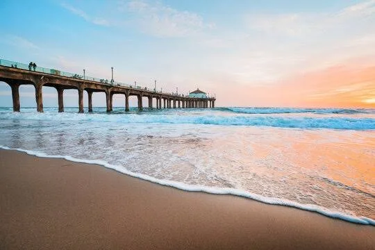 A beach scene with a pier extending into the ocean at sunset, waves lapping at the sandy shore.