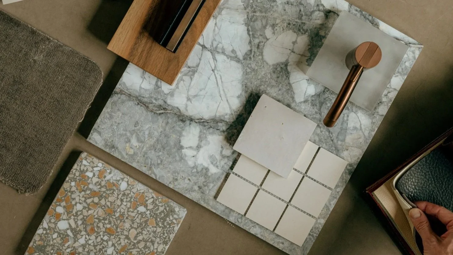 A person selecting tile samples for a project; several tile samples with different textures and colors are spread out on a marble surface.