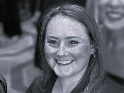 Black-and-white close-up portrait of a woman with medium length dark hair and hoop earrings, smiling warmly at the camera against a softly blurred background.