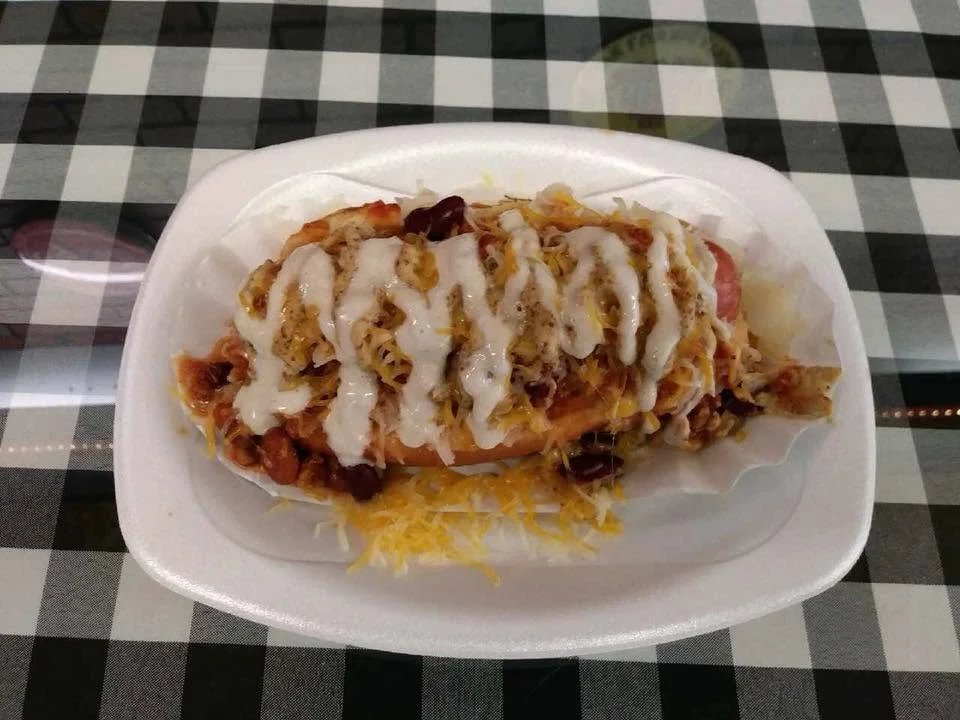 Taco topped with sour cream, cheese, and various fillings, on a white foam plate.