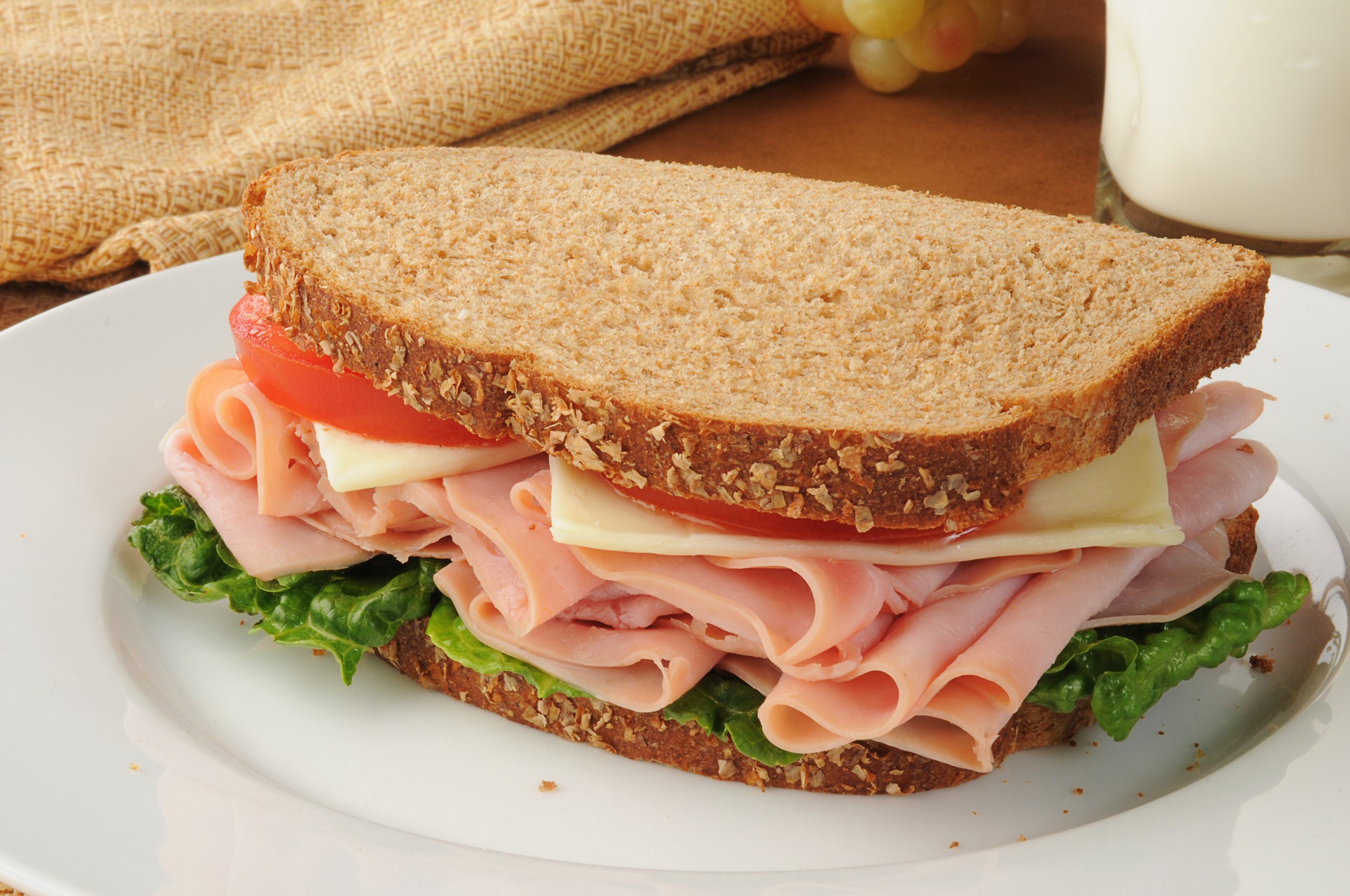 Close-up of a multi-layered sandwich with lettuce, turkey, tomato, cheese, and whole grain bread on a white plate.