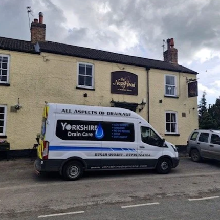 A white van for Yorkshire Drain Care parked in front of a yellow two-story pub with a sign that reads "The Nag's Head."