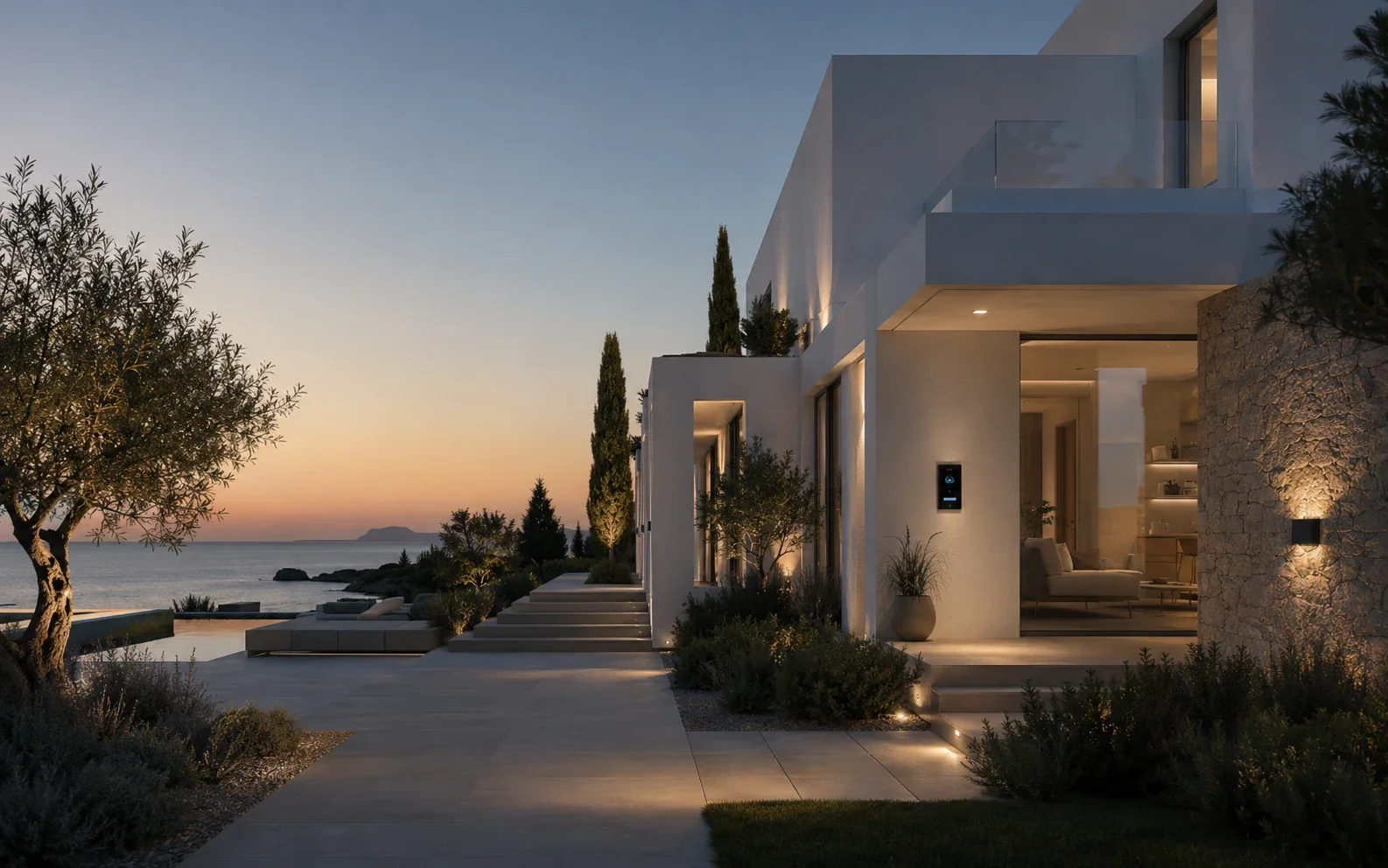 Casa moderna en la playa durante el atardecer, con iluminación exterior y áreas de descanso, rodeada de vegetación y vistas al mar.