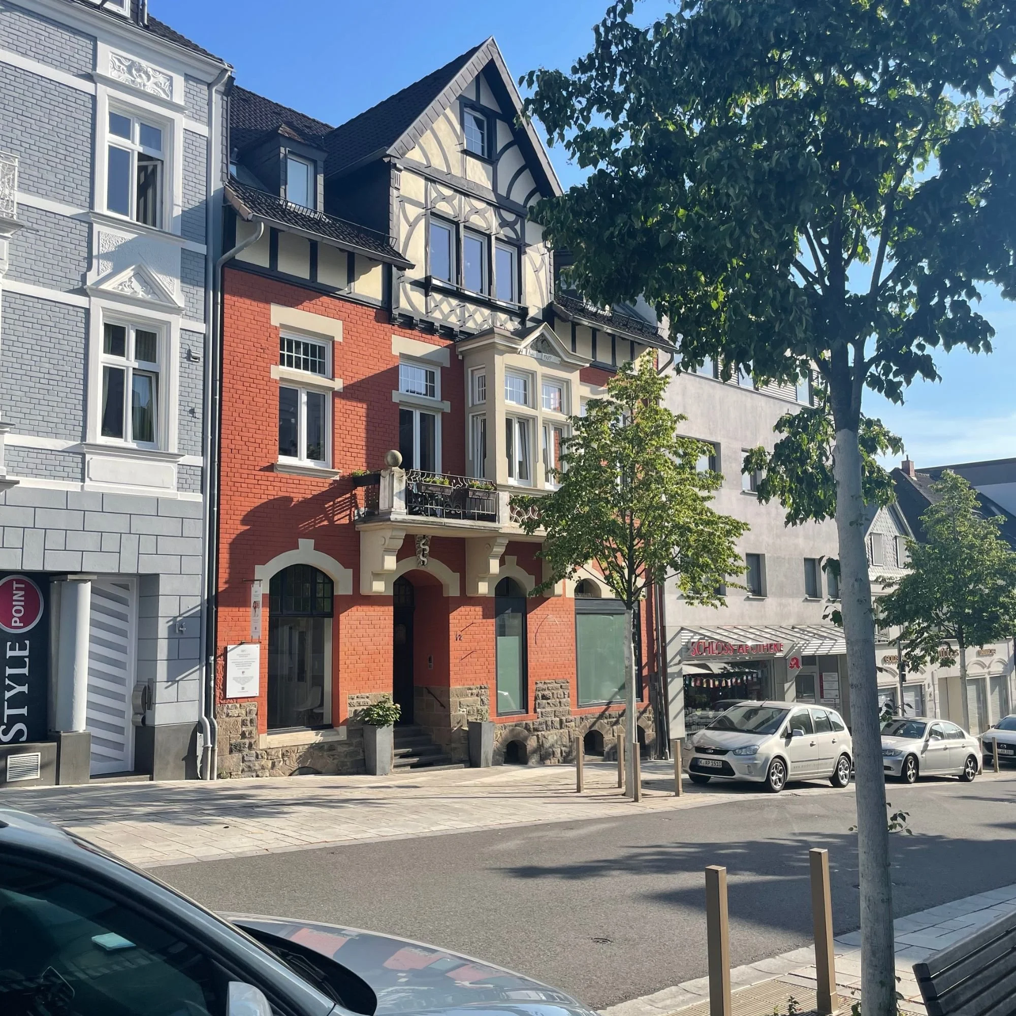 Schloßstraße Bensberg: Straßenansicht mit mehrstöckigem Wohnhaus, Bäumen und parkenden Autos, sonniger Tag.