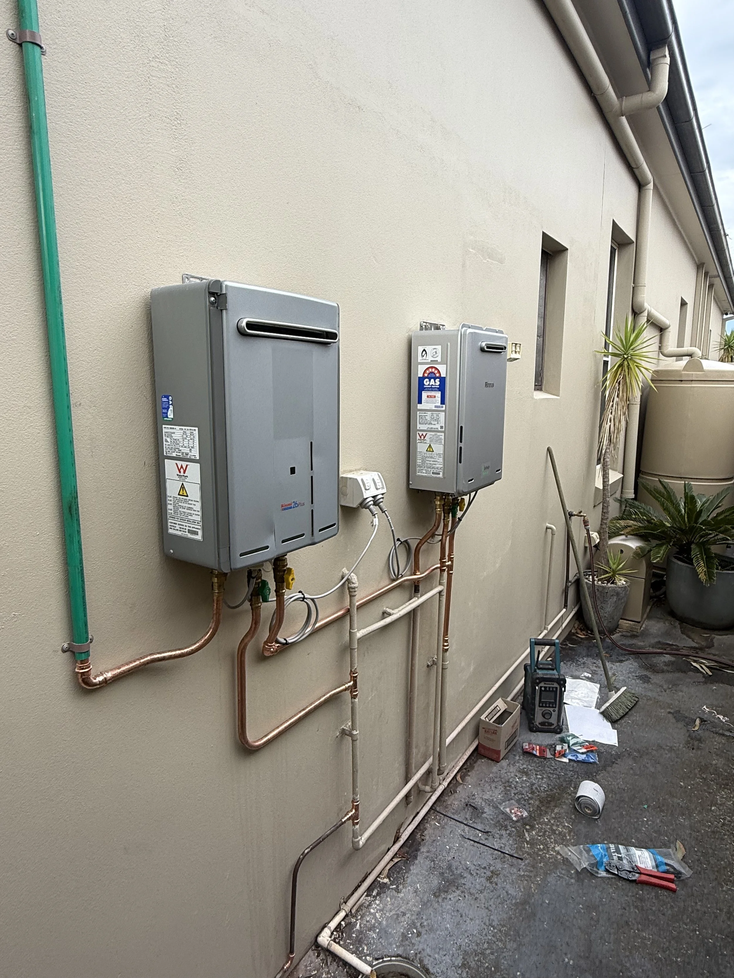 Outdoor wall with electrical and gas meters, with tools and debris scattered on the ground.