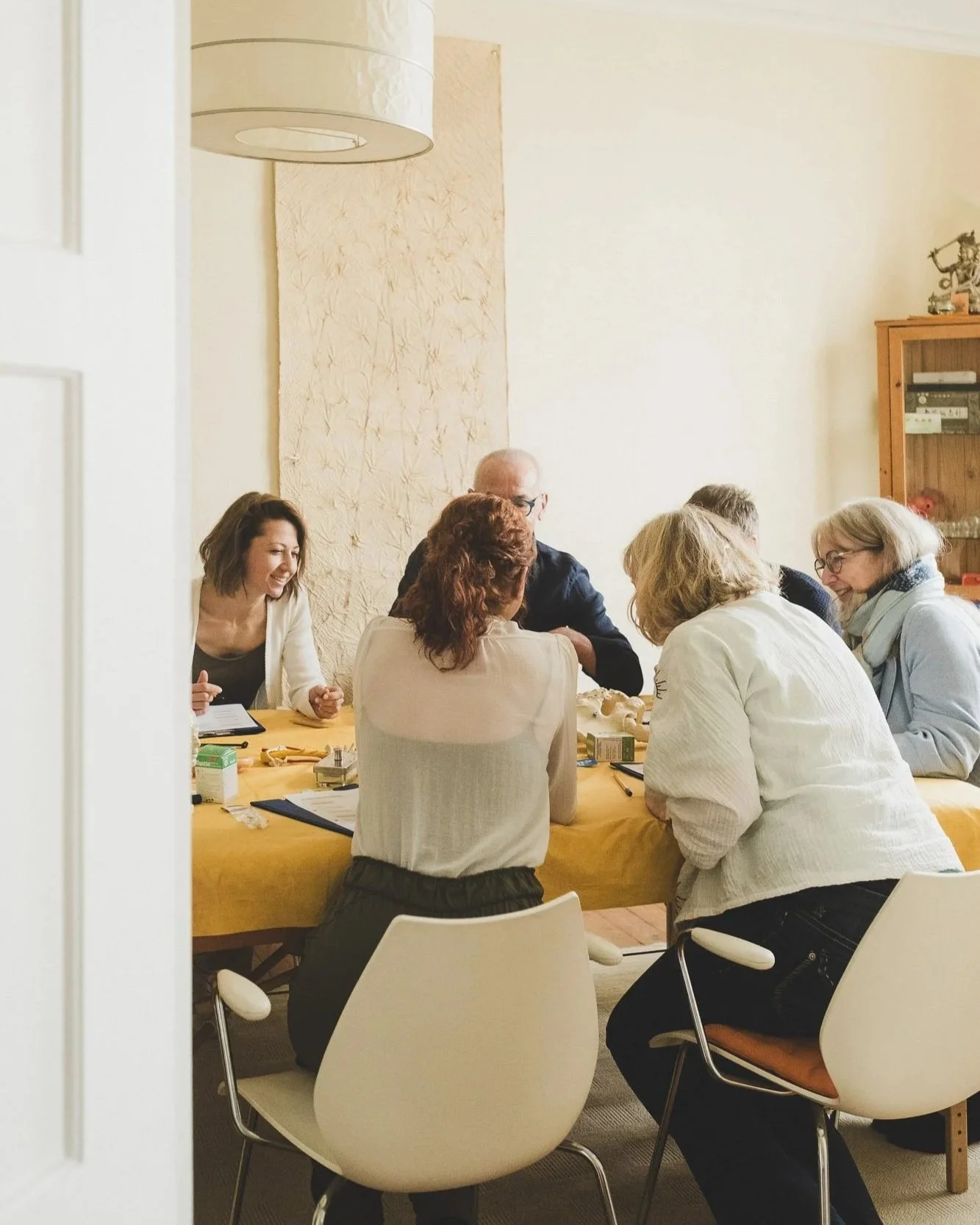 Mehrere Menschen einer Fortbildung sitzen um einen Tisch und unterhalten sich in einem Raum.
