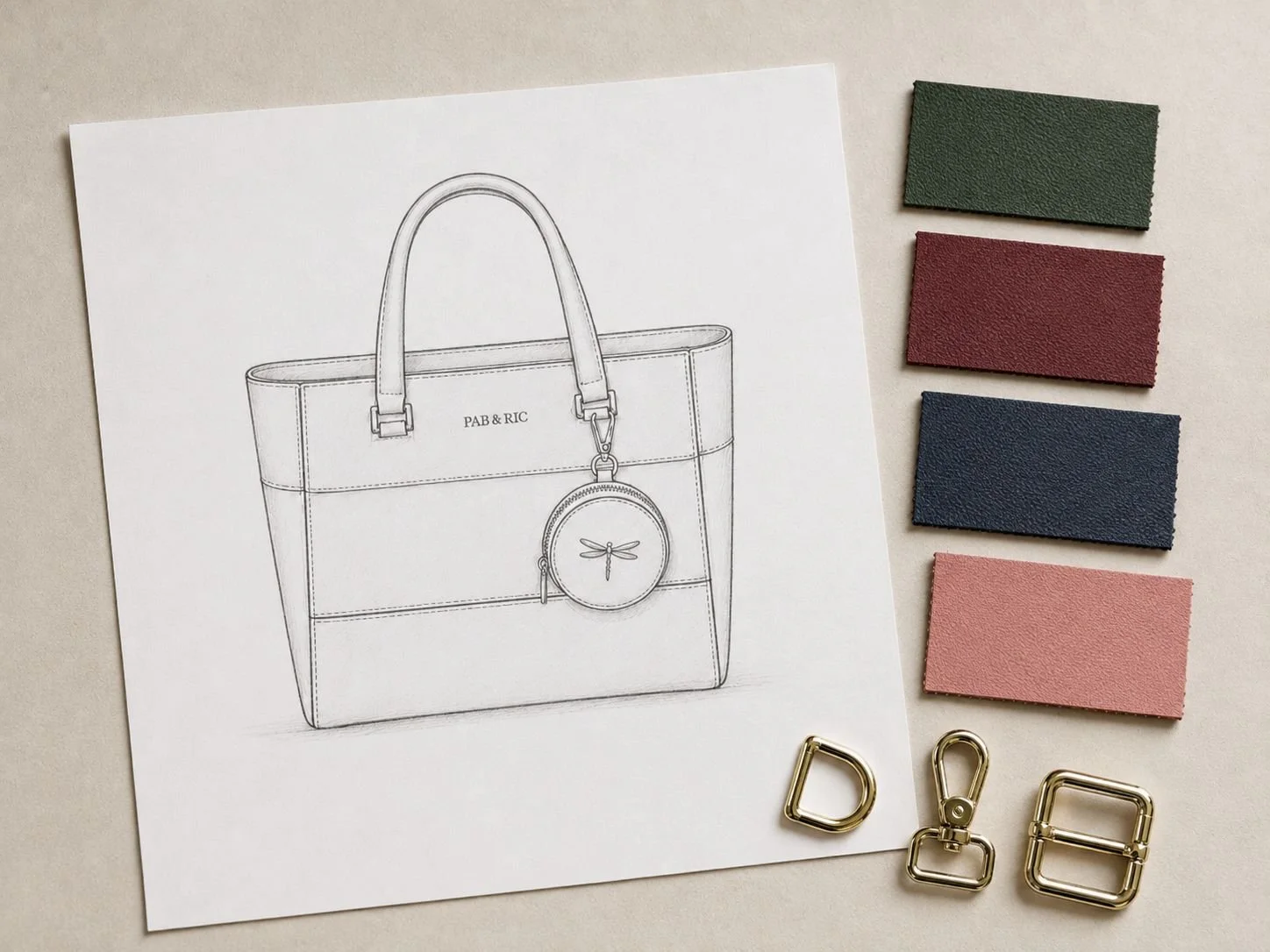 Dibujo de una bolsa de mano en un papel con algunos swatches de colores y herrajes metálicos de calidad.