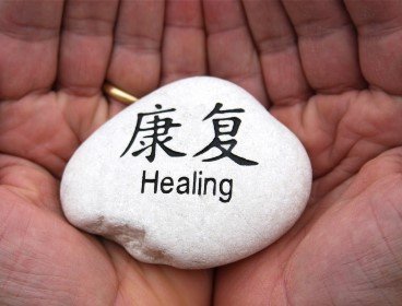 A white stone with the Chinese characters for healing and the English word "Healing" written on it, held by two hands.