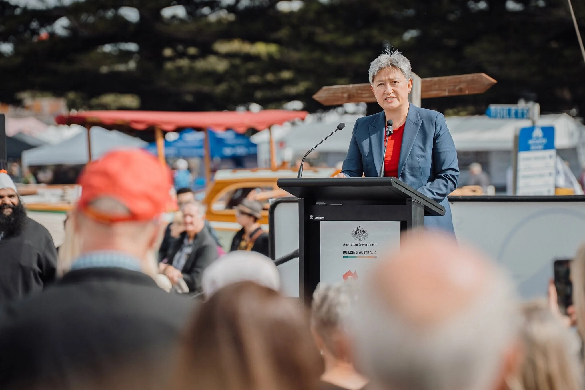 Australian Foreign Minister Senator the Hon Penny Wong speaking at a podium during the 2025 South Australian Wooden Boat Festival with a crowd attending, with tents and trees in the background.
