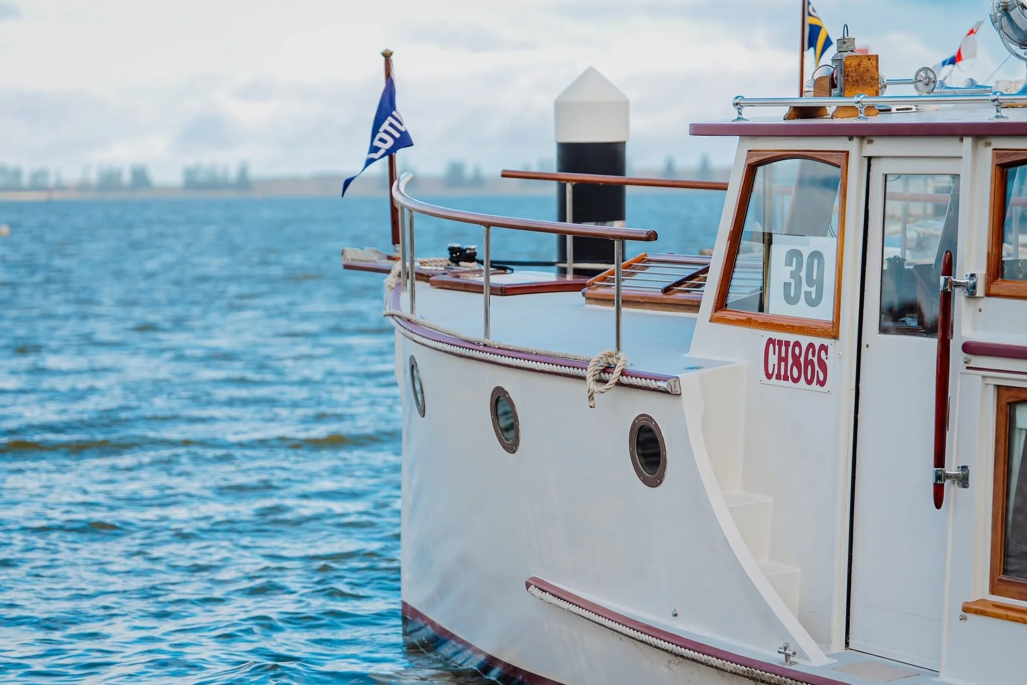 Close-up of a boat's front section with a flag, portholes, and nautical equipment near the water.