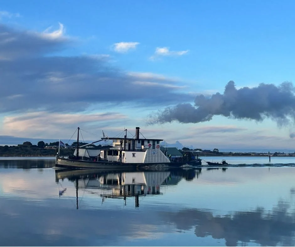 The PS Oscar W on calm water, reflecting the cloudy sky and blue sky above.