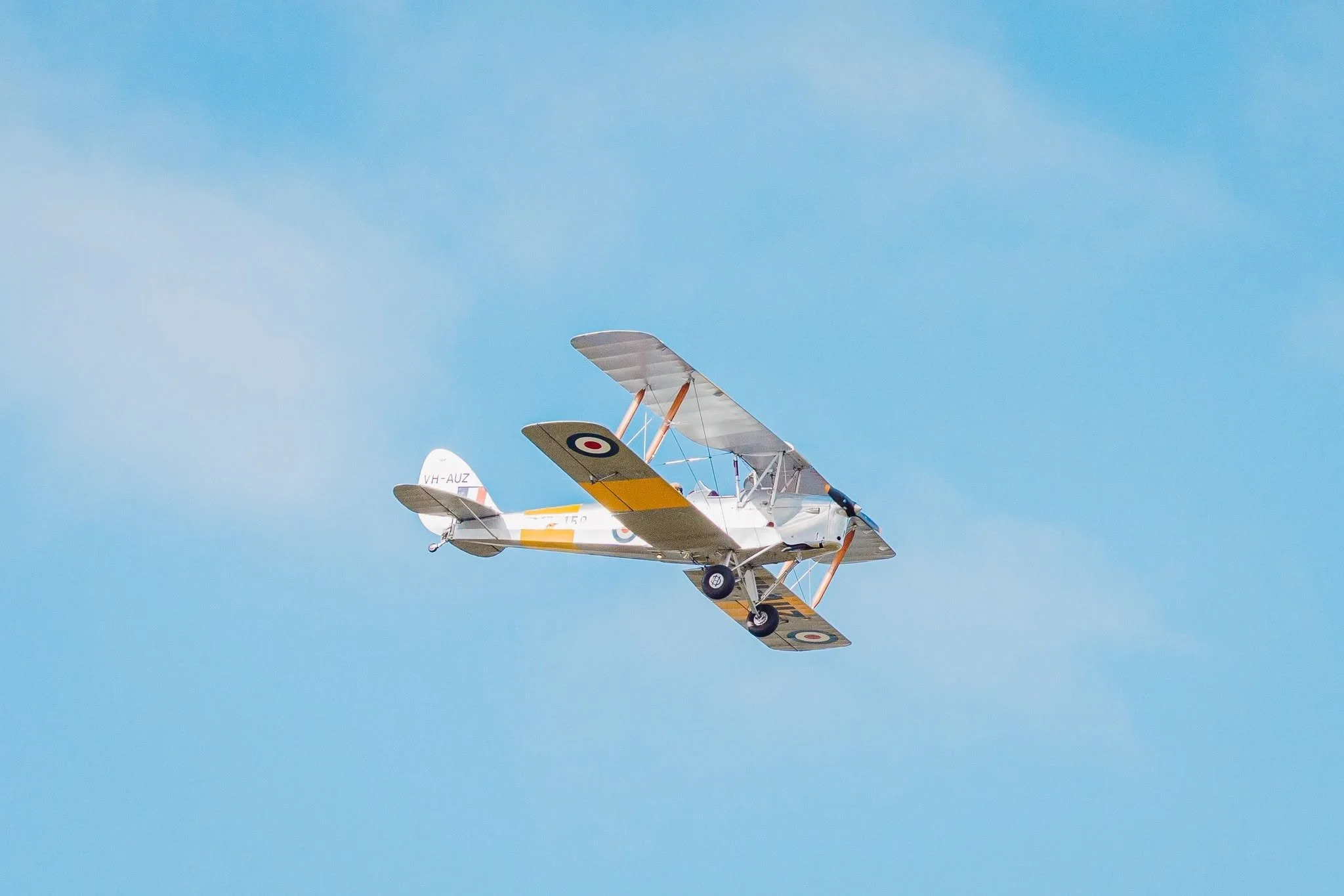 A small vintage biplane flying in a clear blue sky.