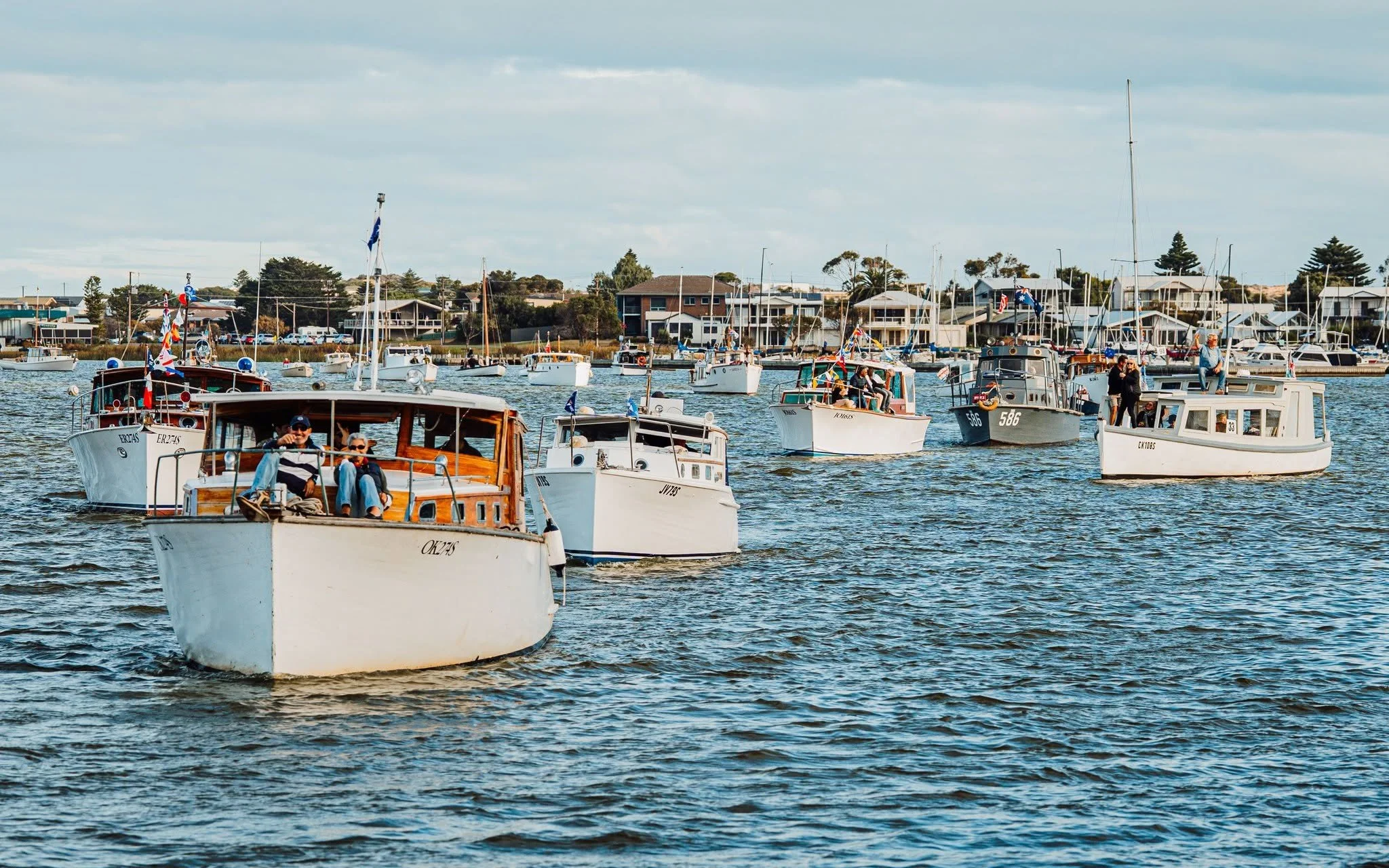 Several boats are sailing on the River Murray with houses and trees in the background.