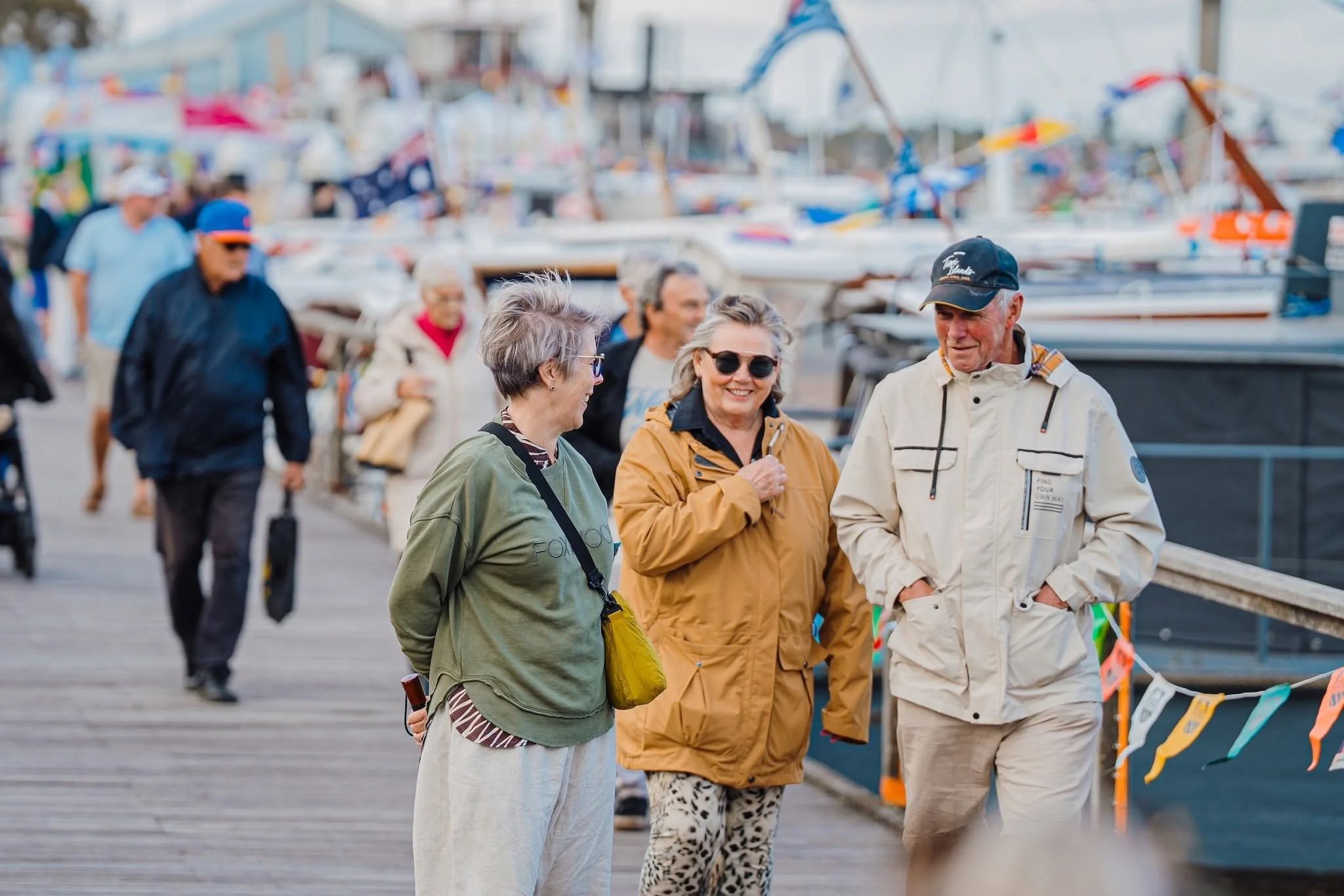 Group of people walking on a dock near boats, smiling and chatting.