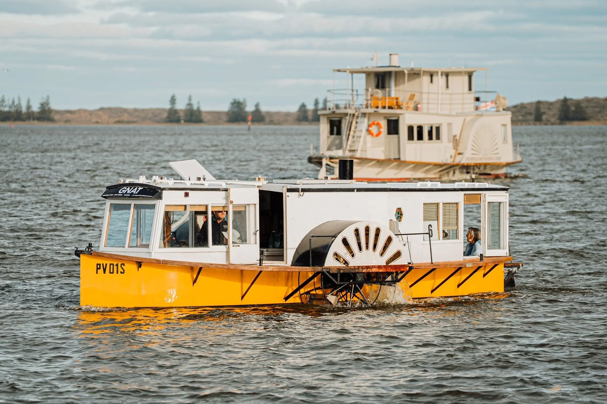 A yellow and white wooden boat with a cabin on the River Murray with a distant shoreline and trees under a partly cloudy sky.