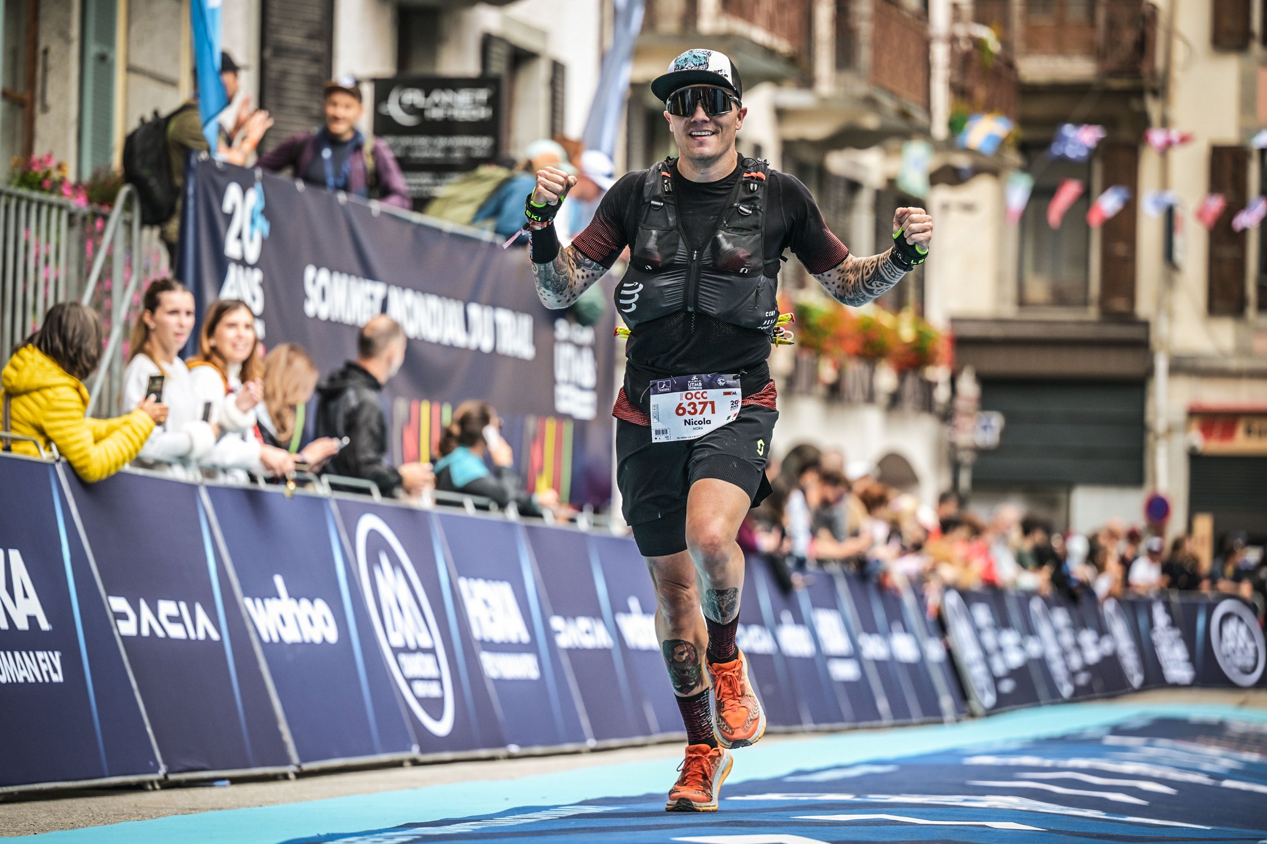 Uomo che corre felice durante una maratona in una strada urbana, con spettatori e bandiere sullo sfondo.