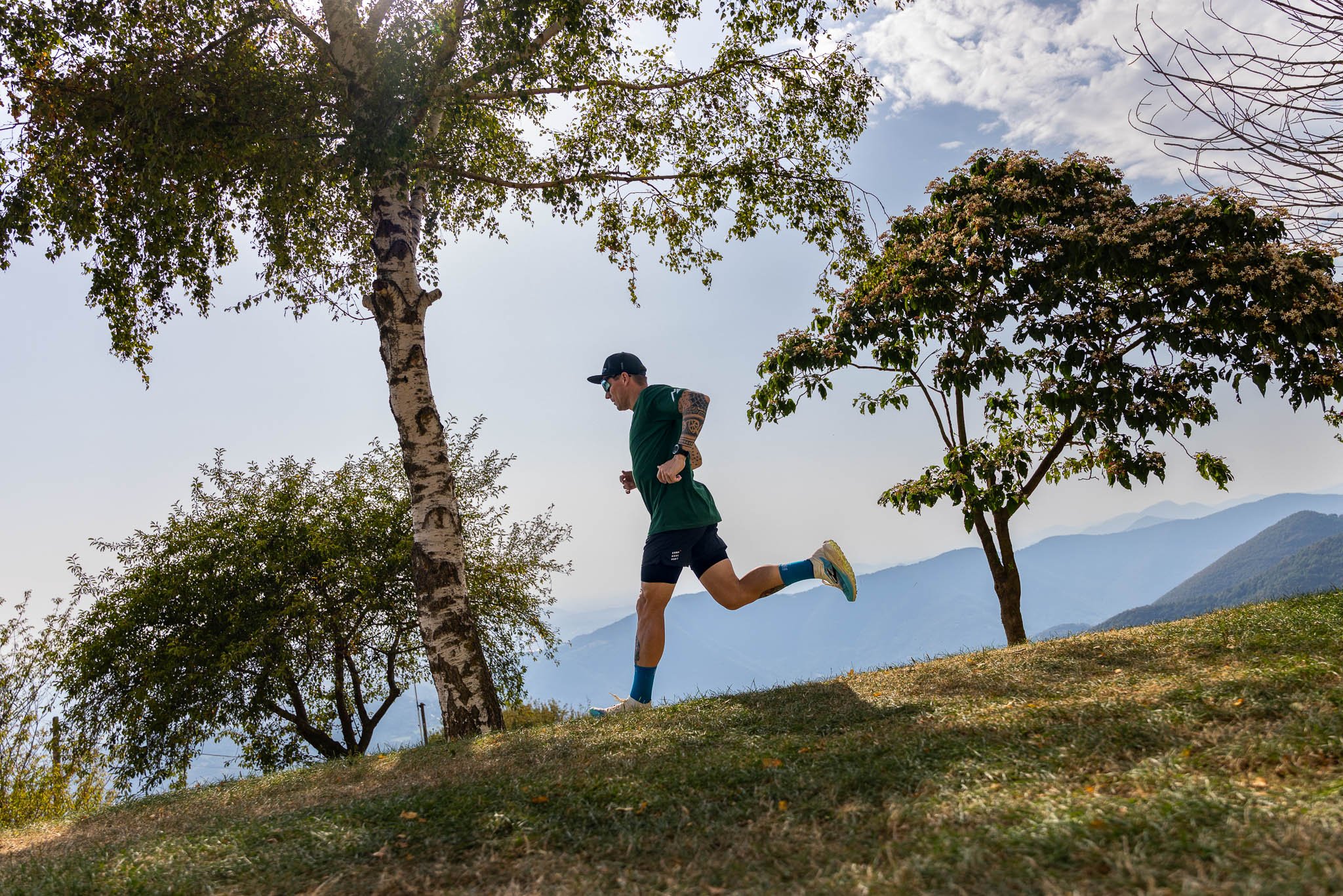 Uomo che corre in un'area naturale con alberi e montagne sullo sfondo.