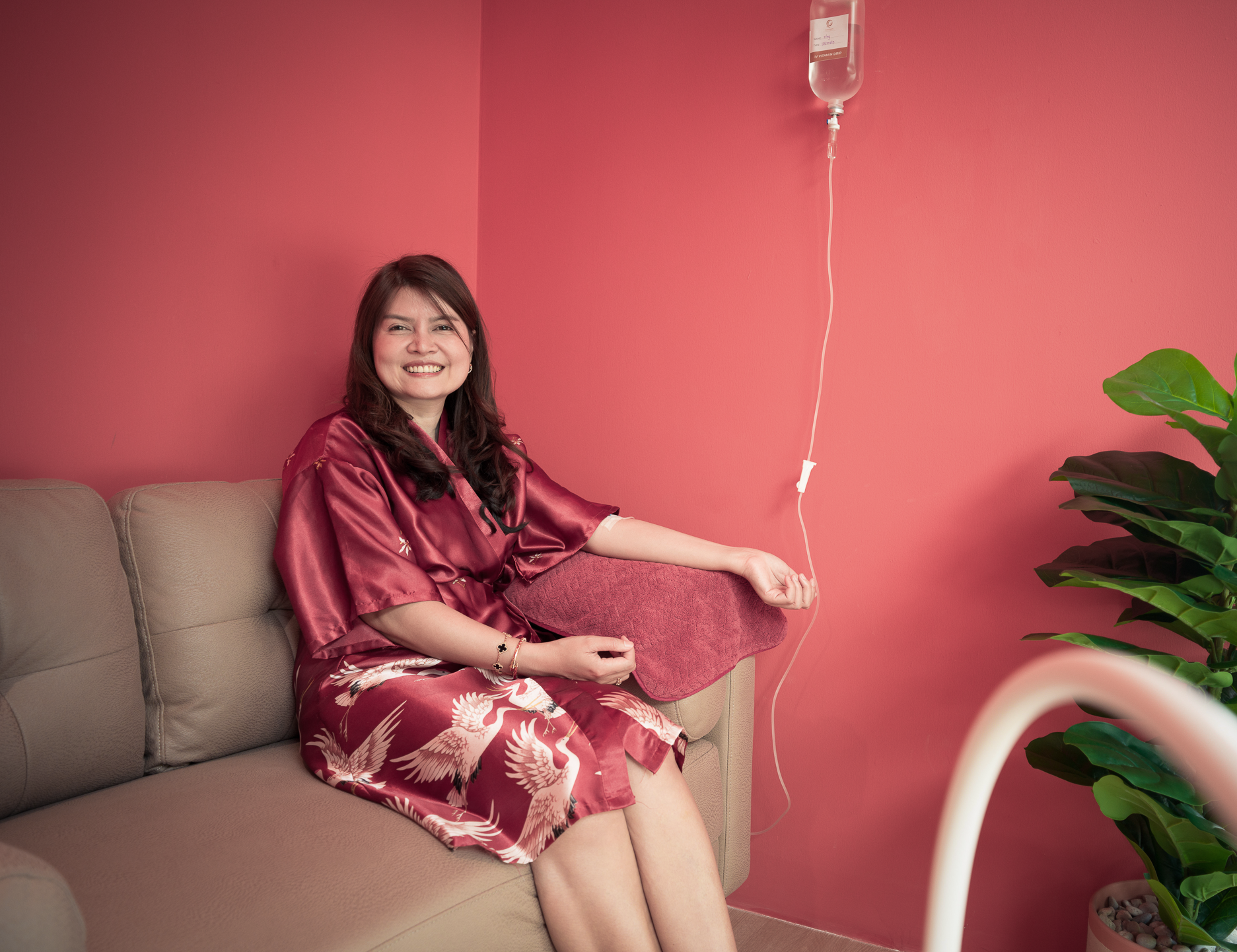 Smiling client in a satin crane-print robe relaxing on a sofa while receiving IV drip therapy in a private cabin at Ponsarin Clinic.
