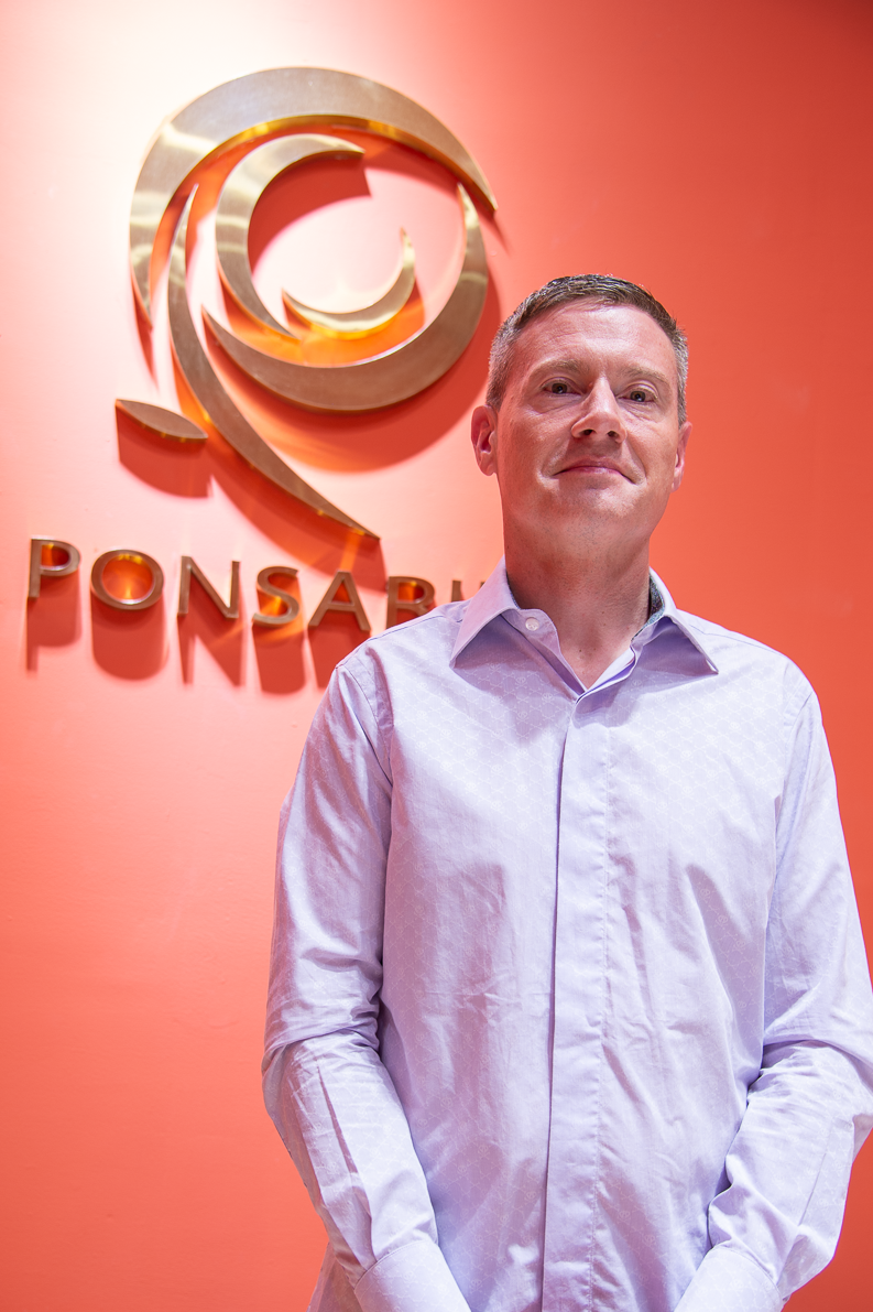 "Smiling man in a blue shirt, featured in a Ponsarin Clinic client testimonial, standing in front of the Ponsarin logo."