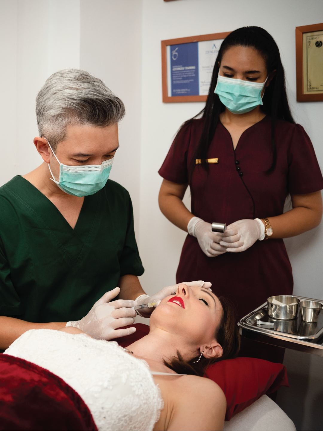 Dr. Sawami of Ponsarin Clinic preparing to administer a filler injection to a client's face, with a masked assistant holding supplies nearby.