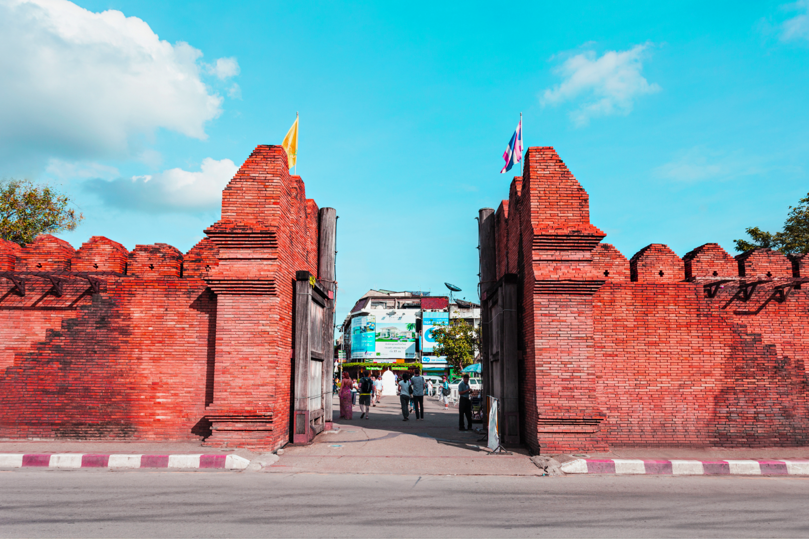 Tha Phae Gate, the iconic ancient brick city wall entrance in Chiang Mai, near Ponsarin Clinic, with pedestrians walking through under a blue sky.