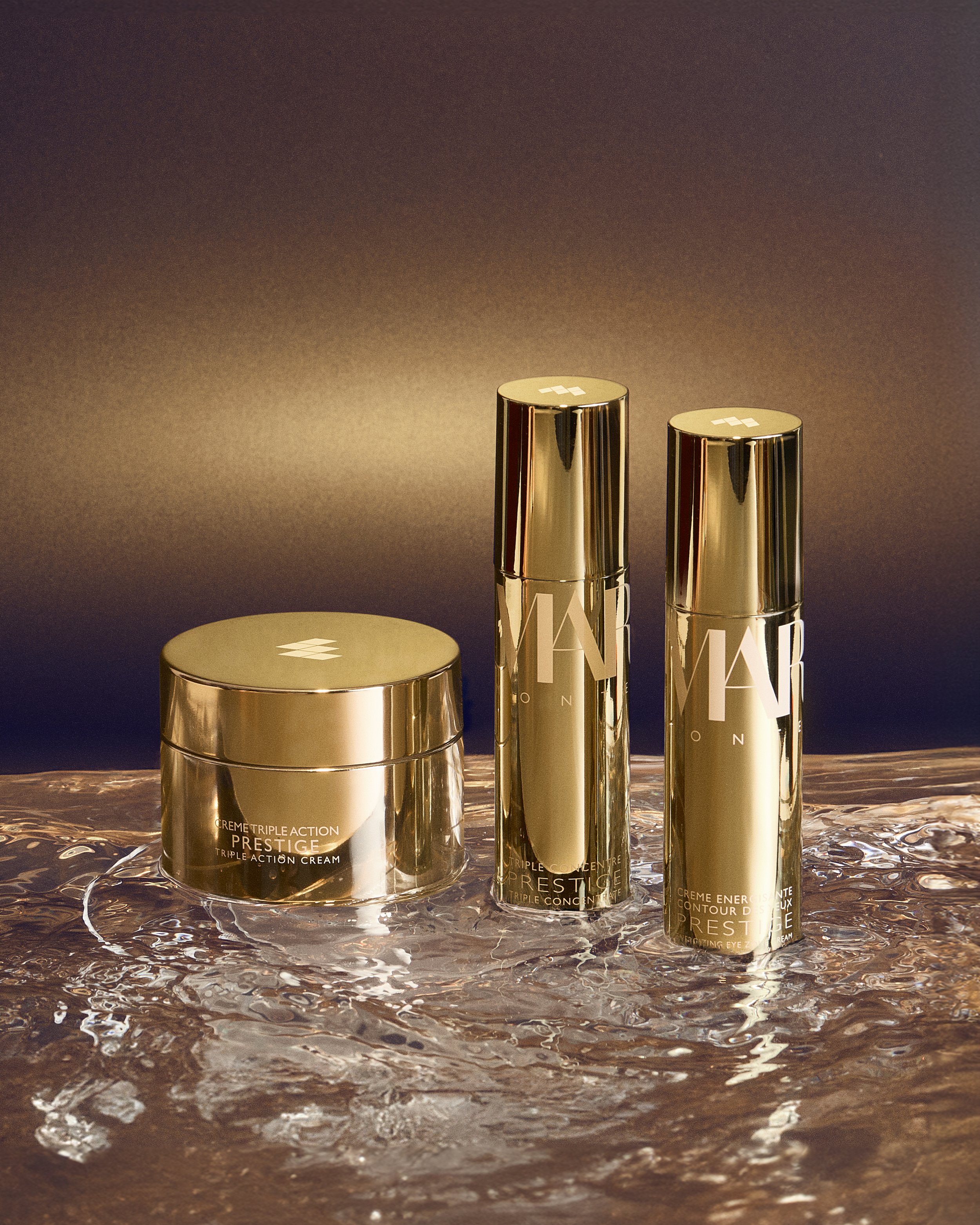 Margy's Monte Carlo Prestige skincare range in gold packaging, featuring a jar and two pump bottles on a marble surface.