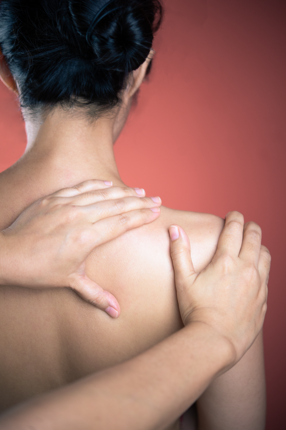 Close-up of a therapist's hands massaging a client's neck and shoulders during a treatment at Ponsarin clinic, with a coral-pink backdrop.