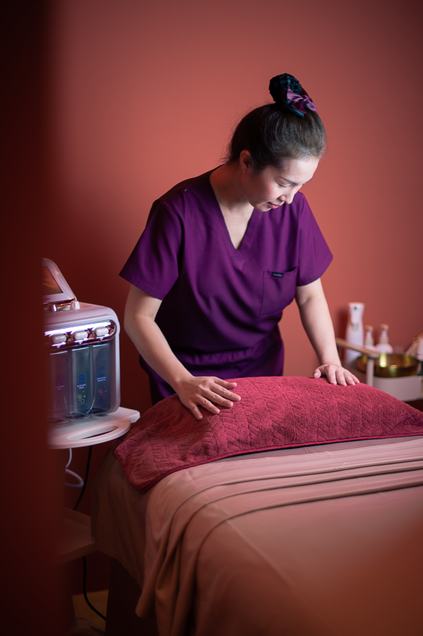 Ponsarin clinic therapist in purple scrubs arranging a towel on a treatment bed while preparing a private cabin.