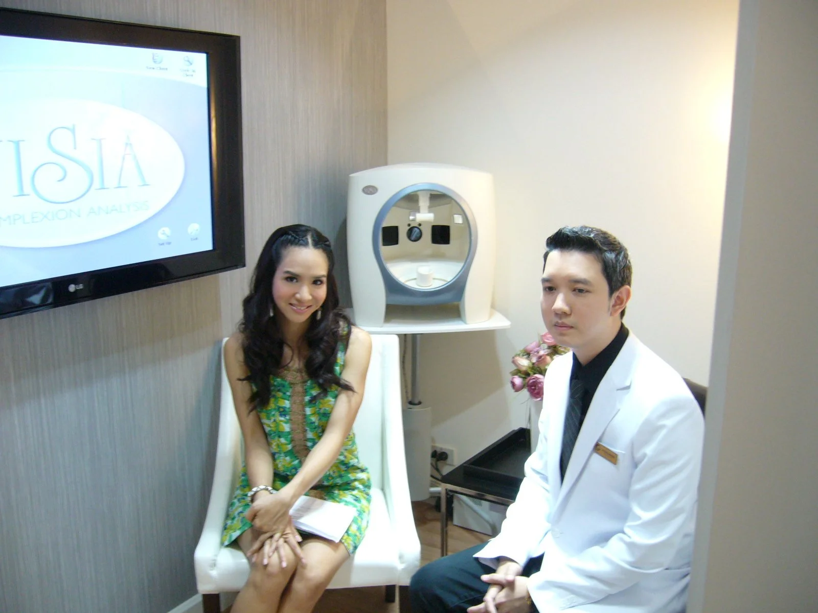 Ponsarin Clinic doctor seated beside a smiling client next to a skin analysis device, with a screen showing skin complexion analysis software in the background.