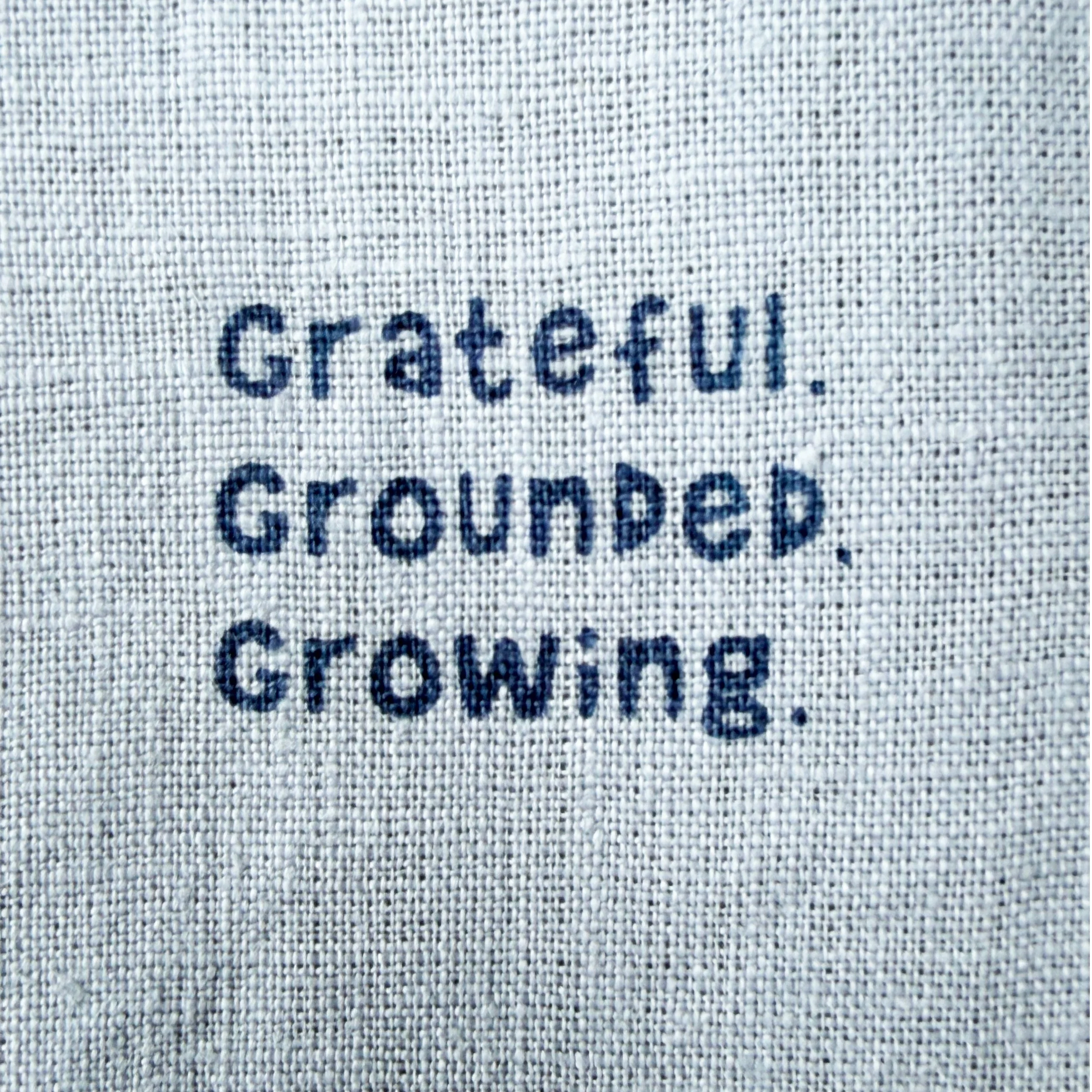 Förstorad bild av texten 'Grateful, Grounded, Growing på ett tyg.