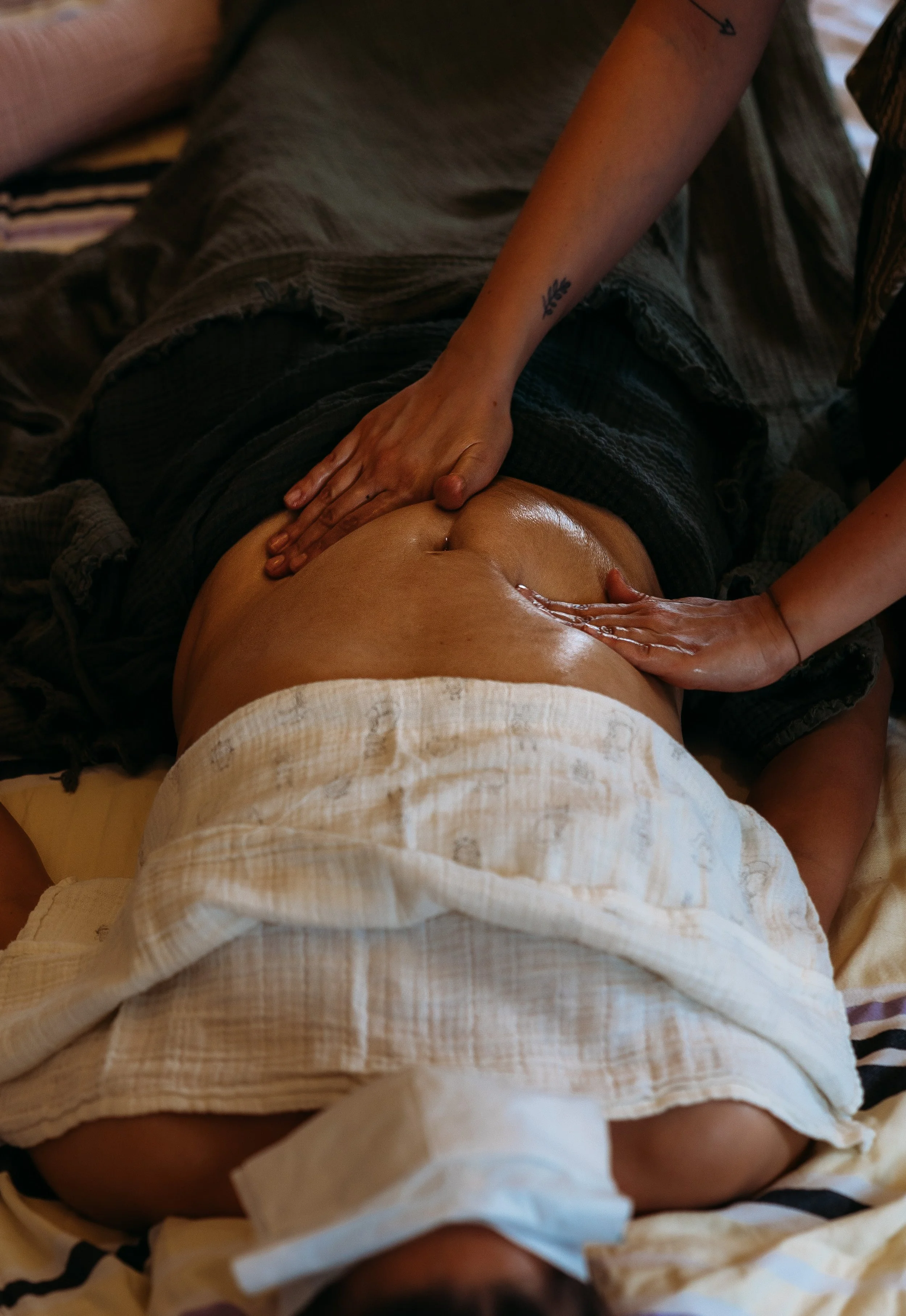 Nahaufnahme einer Person, die eine Massage an ihrem Bauch erhält, mit sichtbaren Händen, die den Bauch sanft berühren, in einem entspannten, warmen Raum.
