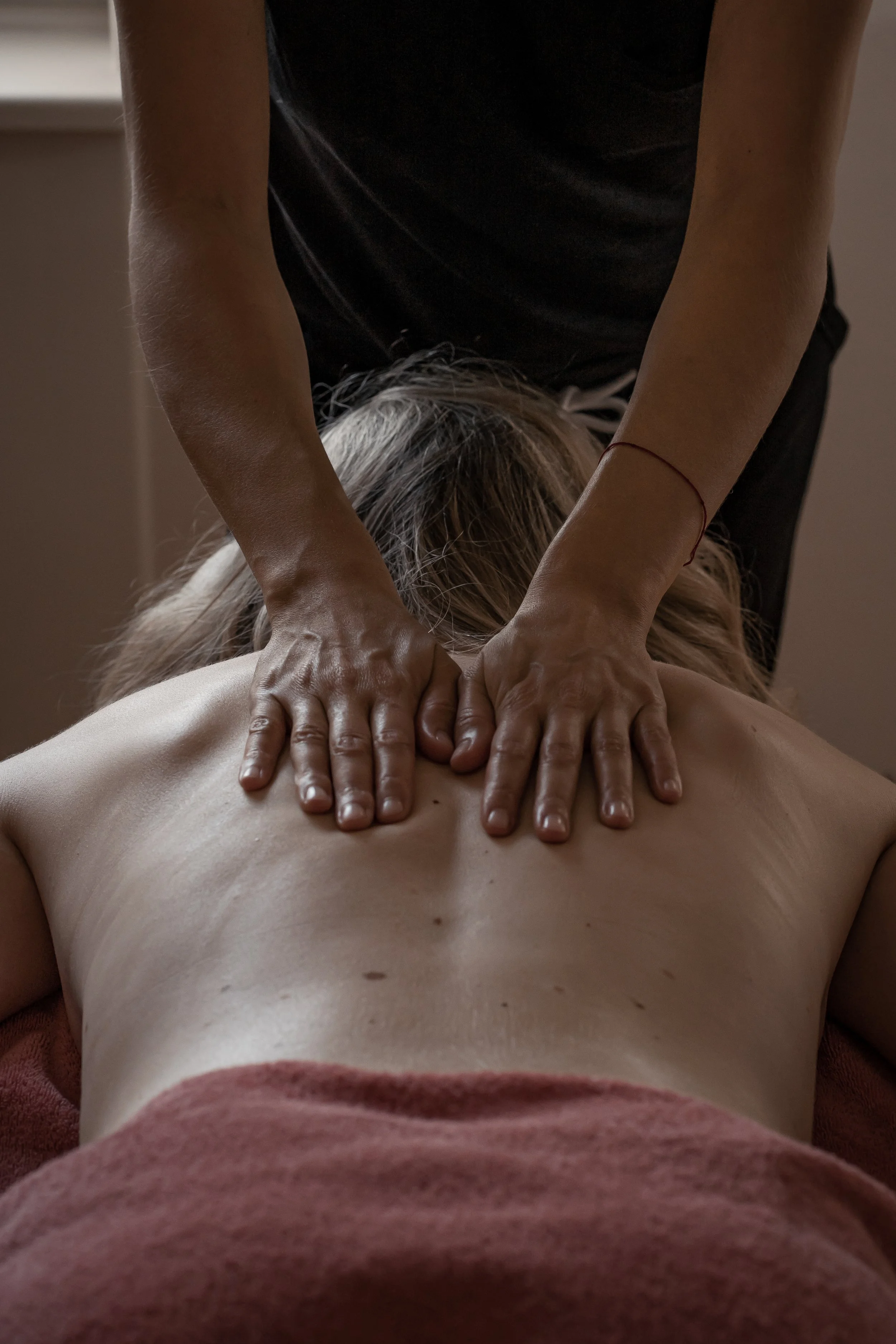Nahaufnahme einer Massage, bei der eine Person den Rücken eines anderen Menschen massiert, der nackt ist, mit einem dunklen Handtuch bedeckt.