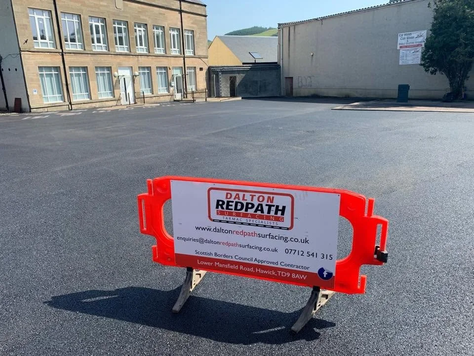 A parking lot with an orange barricade that has sign for Dalton Redpath Surfacing on it, indicating road work or surface work in progress.