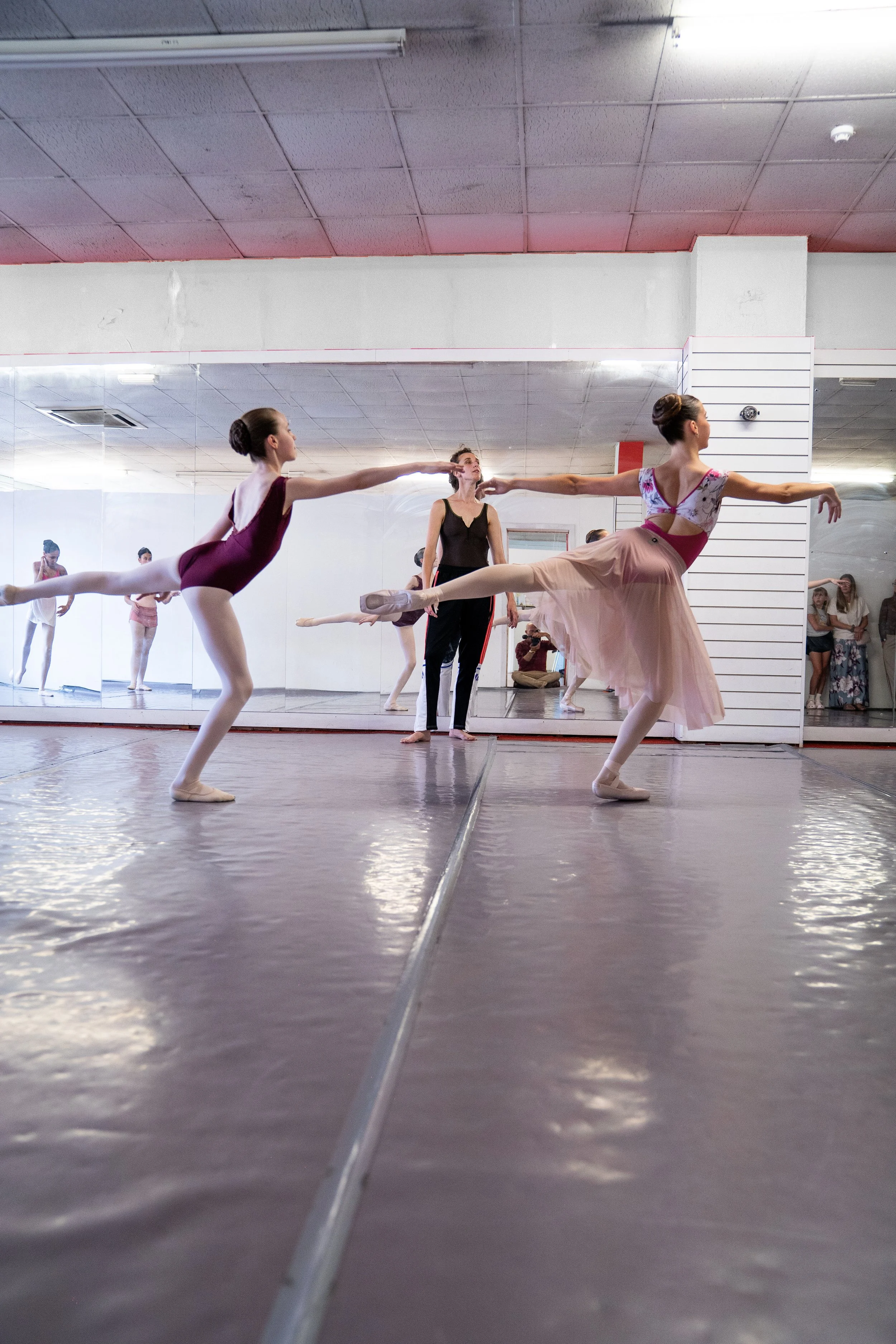 Ballet dancers practicing in a dance studio with a mirror, with some watching from the side.