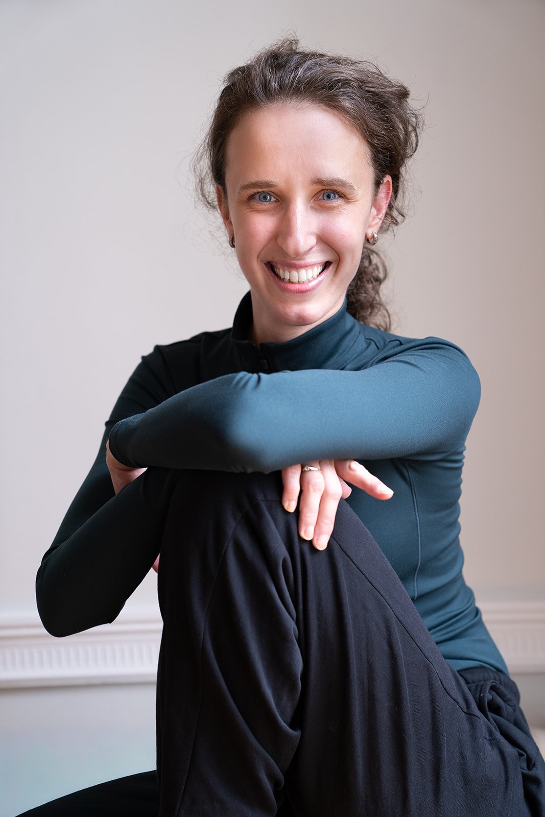 Ballet coach Emma Layne smiling in dancewear while seated for a studio portrait.