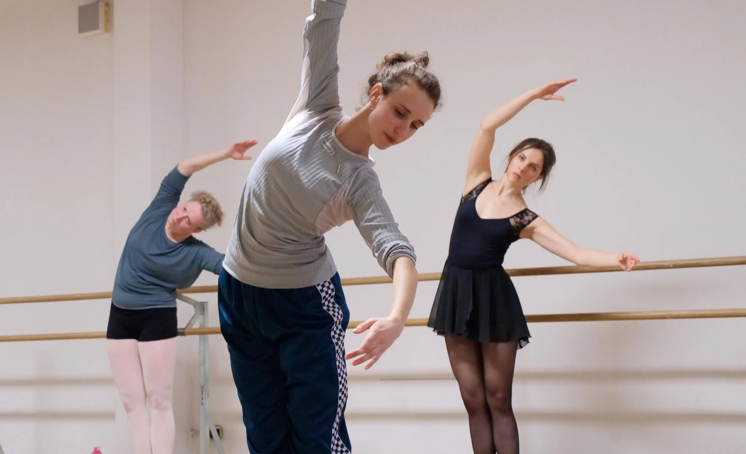 Ballet dancers practising together at the barre during a studio class.