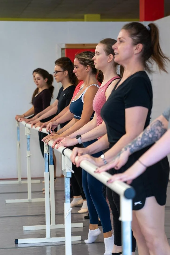 Ballet students practicing at a barre in a dance studio.
