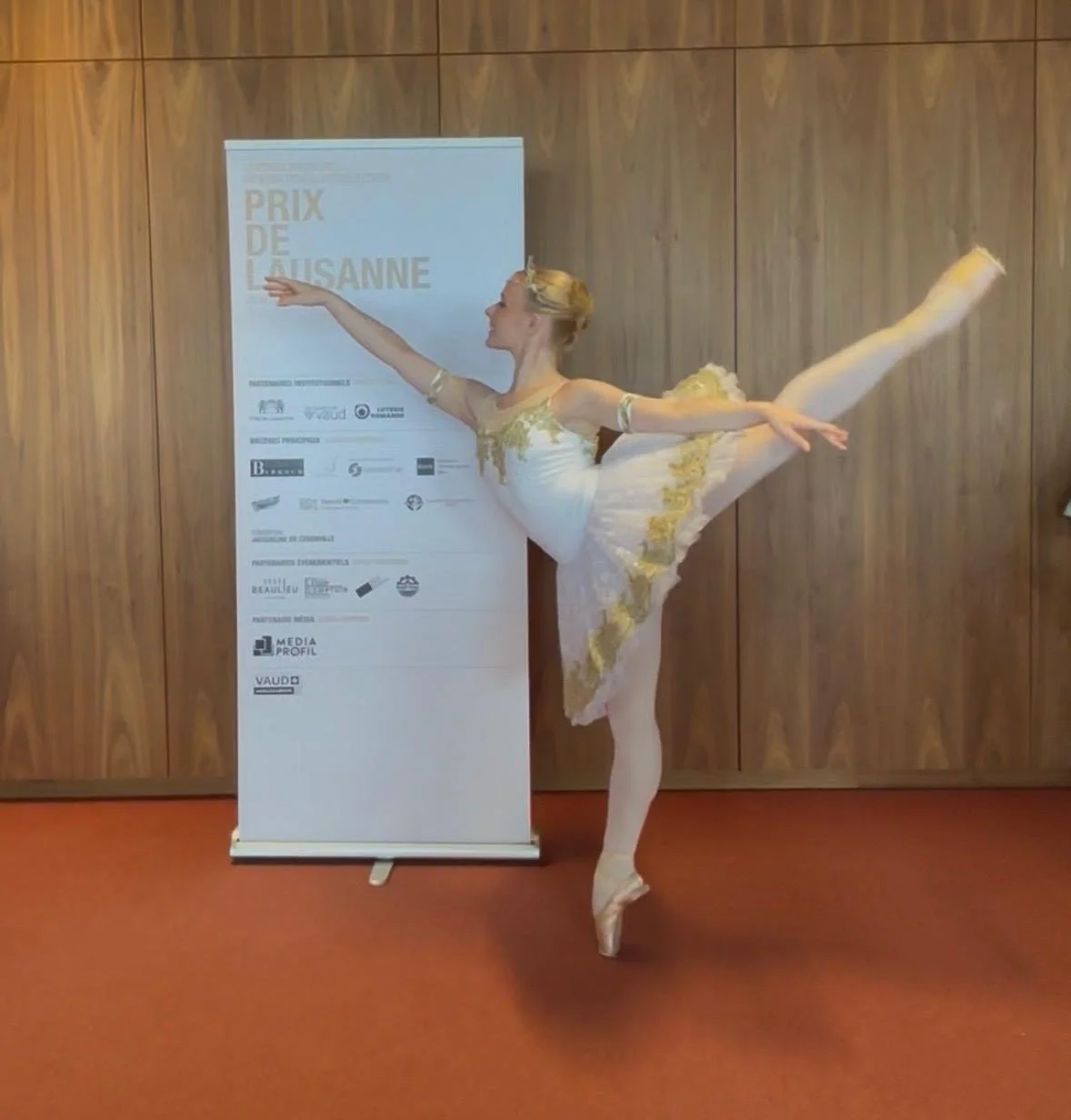 Ballet dancer practicing alone in a dance studio with a dark floor and black walls.