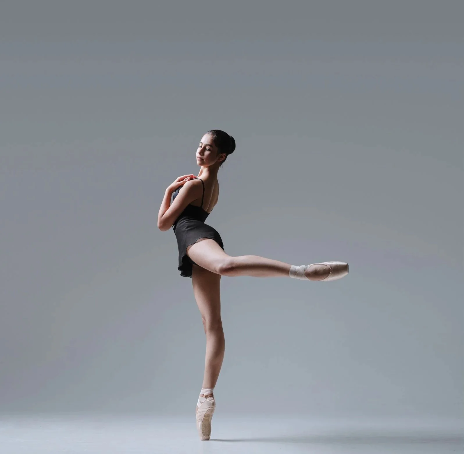 Ballet dancer performing an arabesque en pointe in a black leotard.